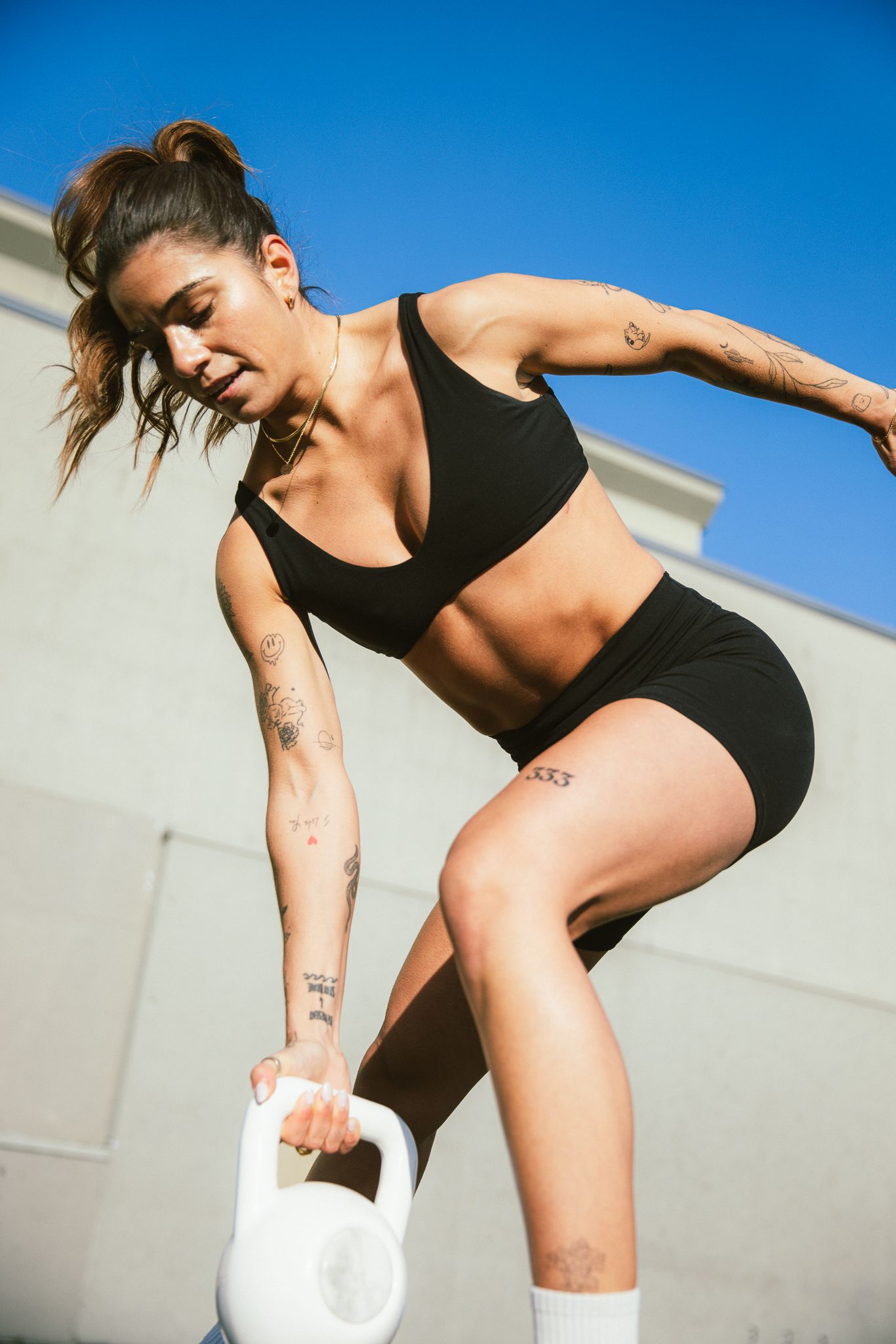 Tattooed female athlete in black sportswear performing a single-leg kettlebell exercise outdoors.