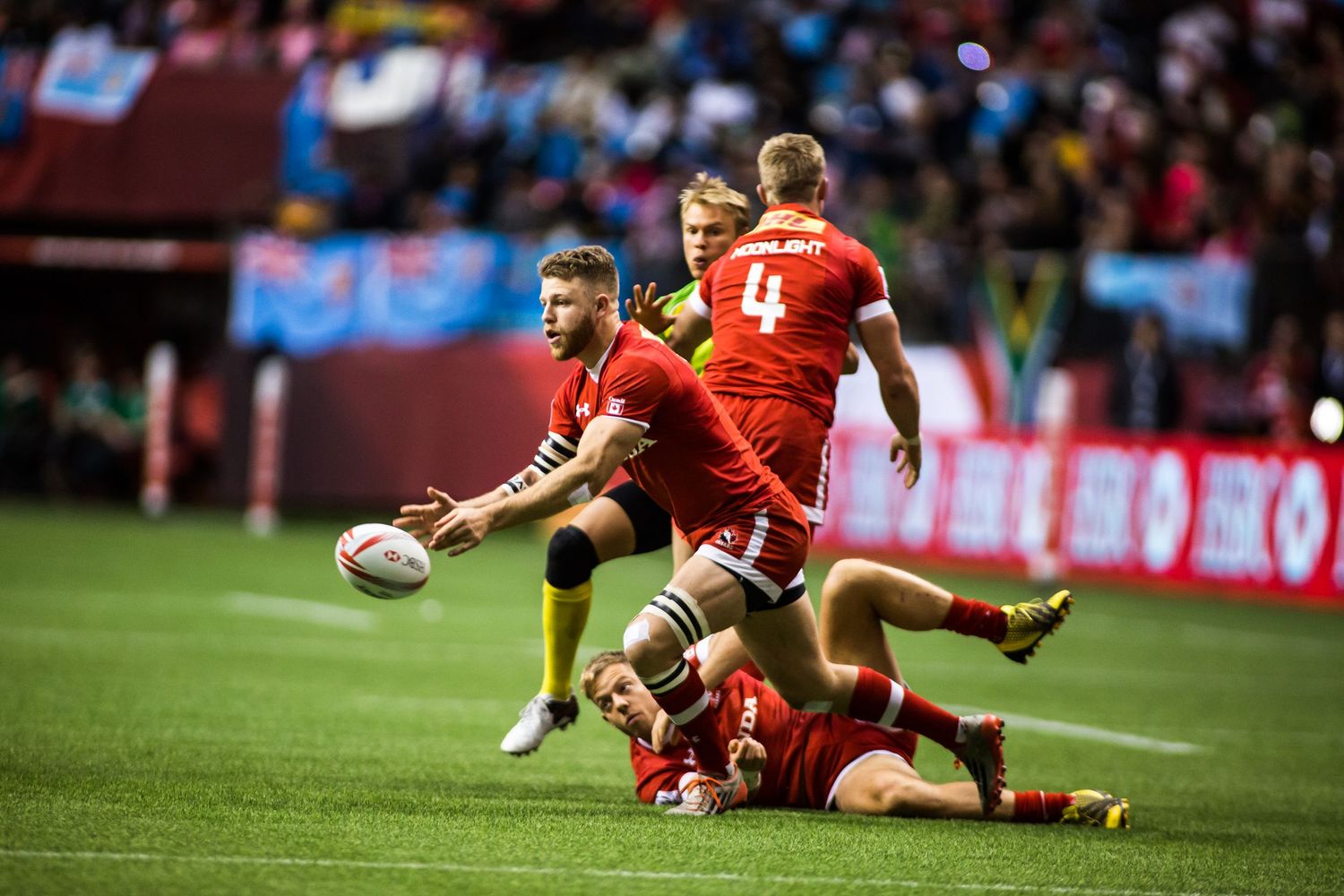 Rugby players in red jerseys compete intensely on the field during a professional sevens tournament match.