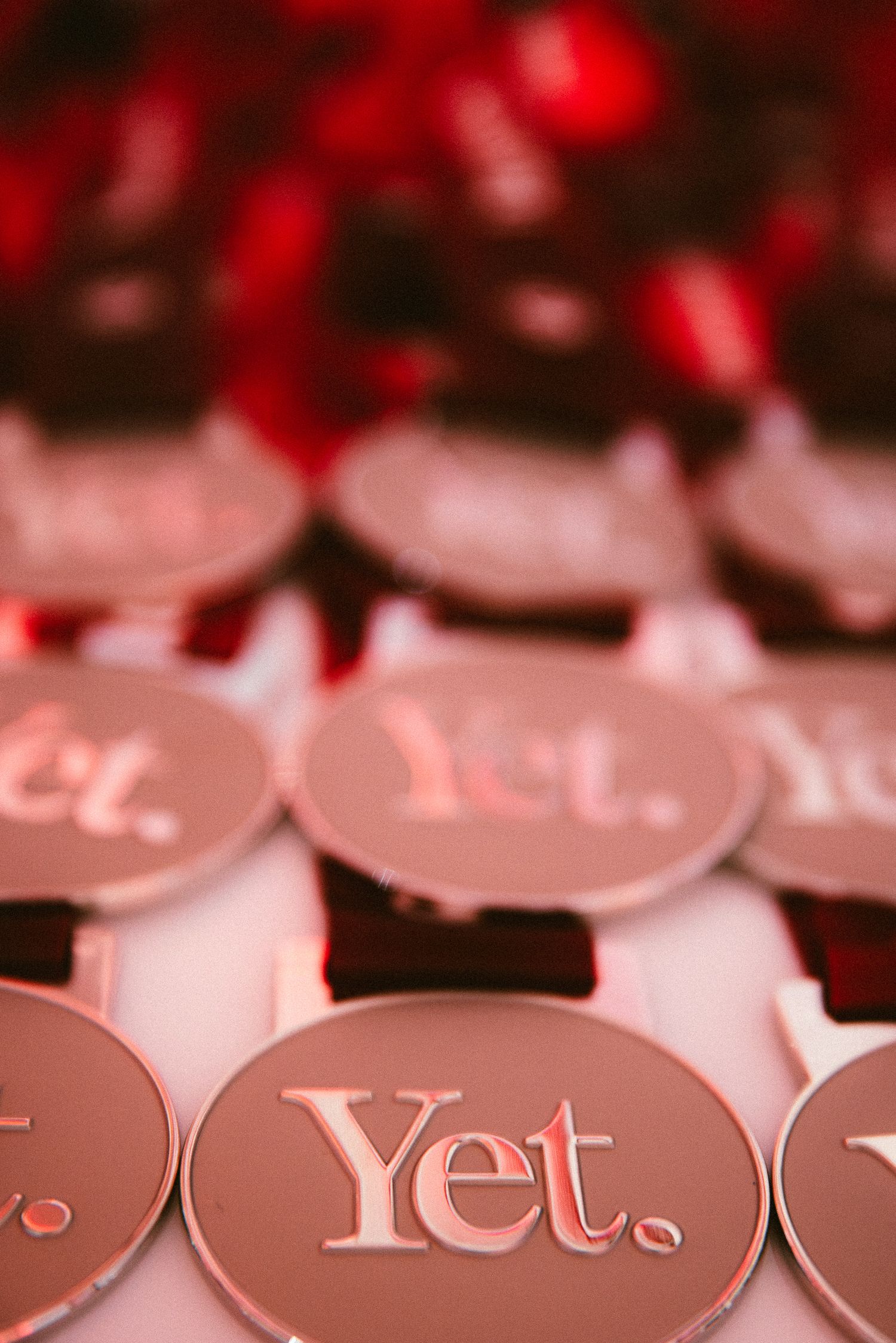 Close-up of shiny round metallic coins engraved with the word Yet. arranged in rows under red lighting.