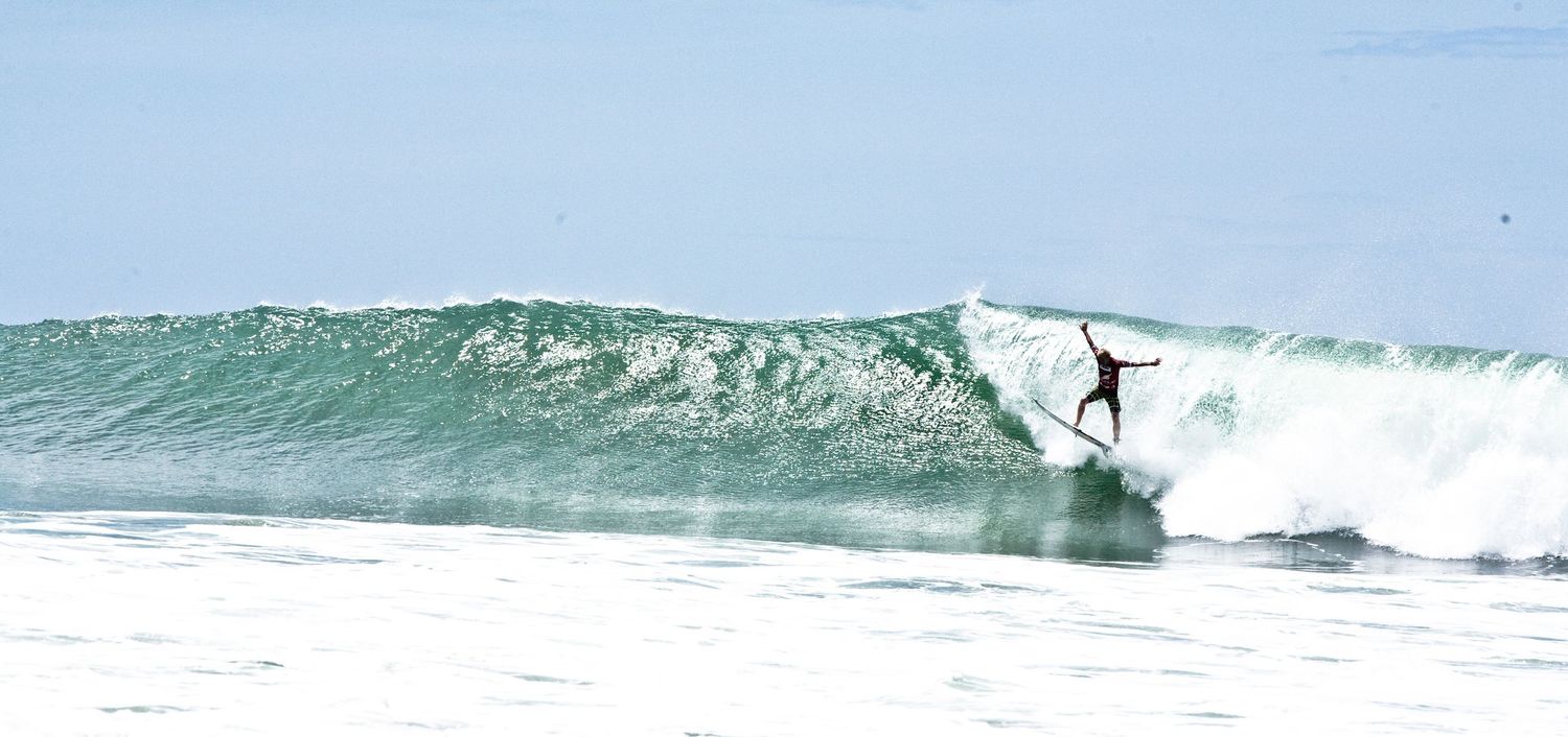 Surfer performing a maneuver on a tall curling ocean wave on a clear day.
