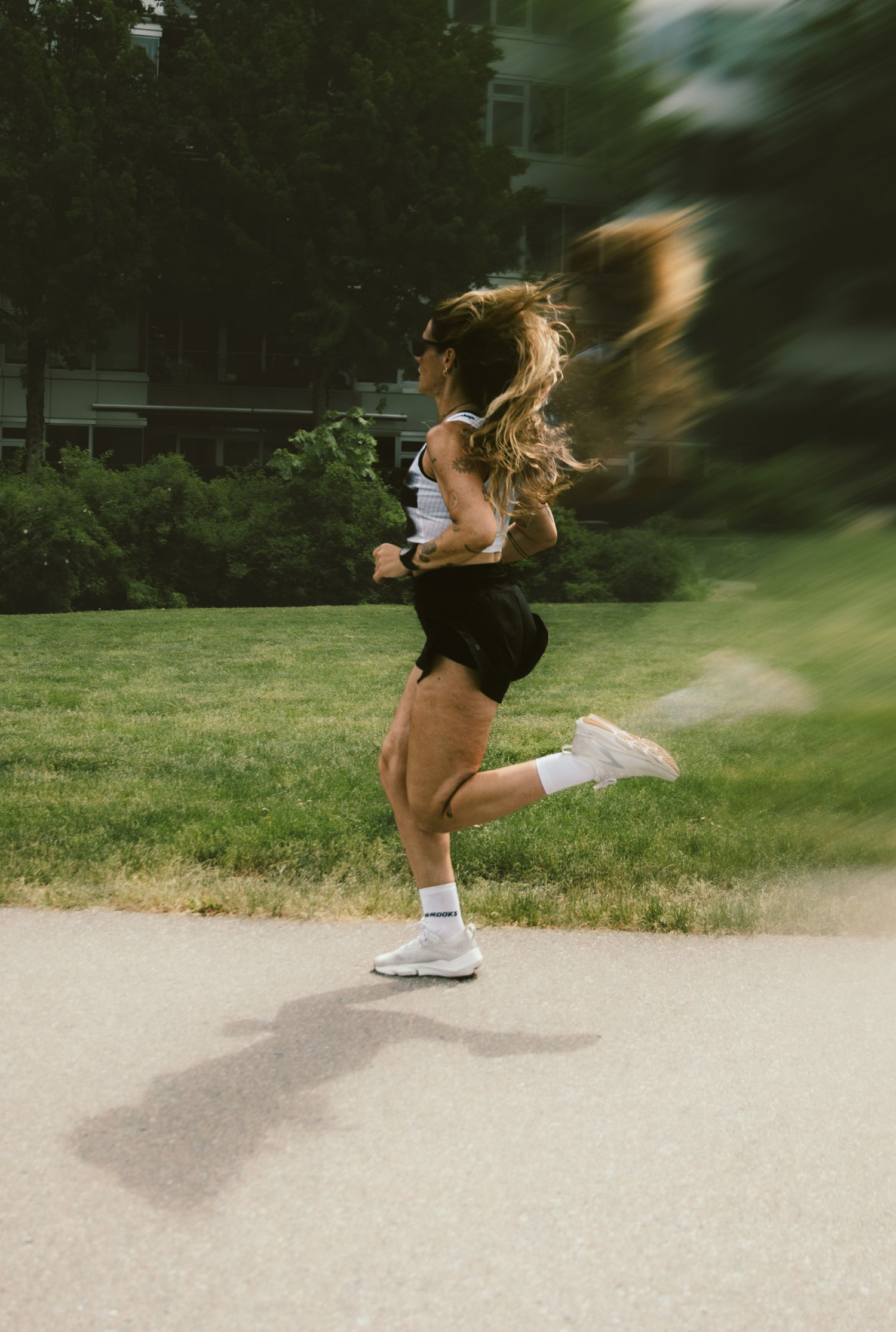 Woman with ponytail running in park wearing white tank top and black shorts.
