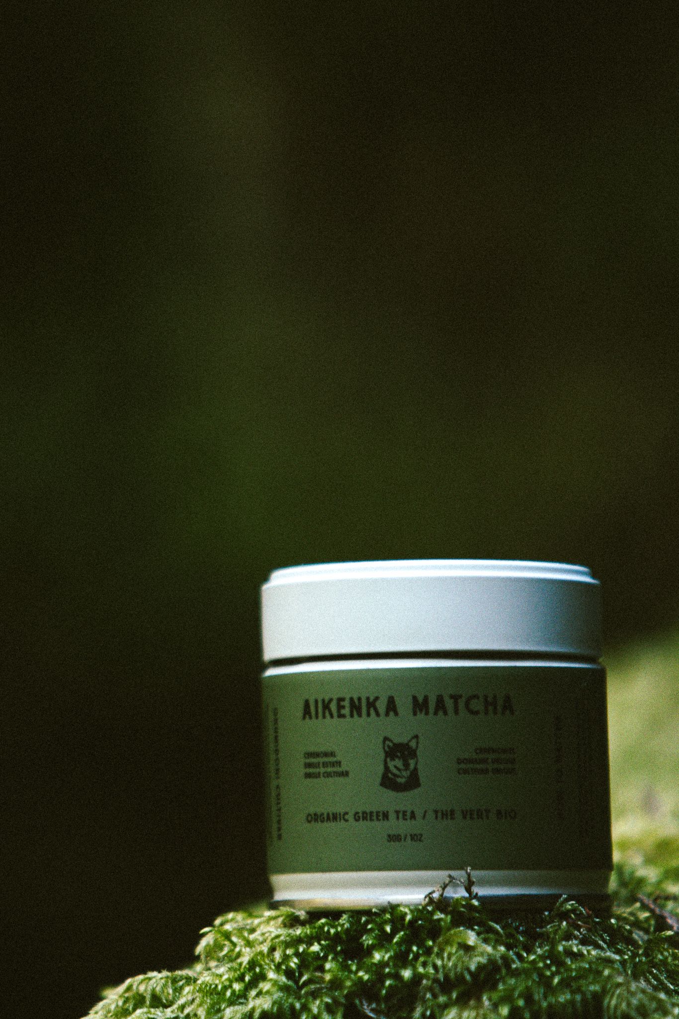Aikenka Matcha organic green tea tin resting on moss-covered surface in natural setting.