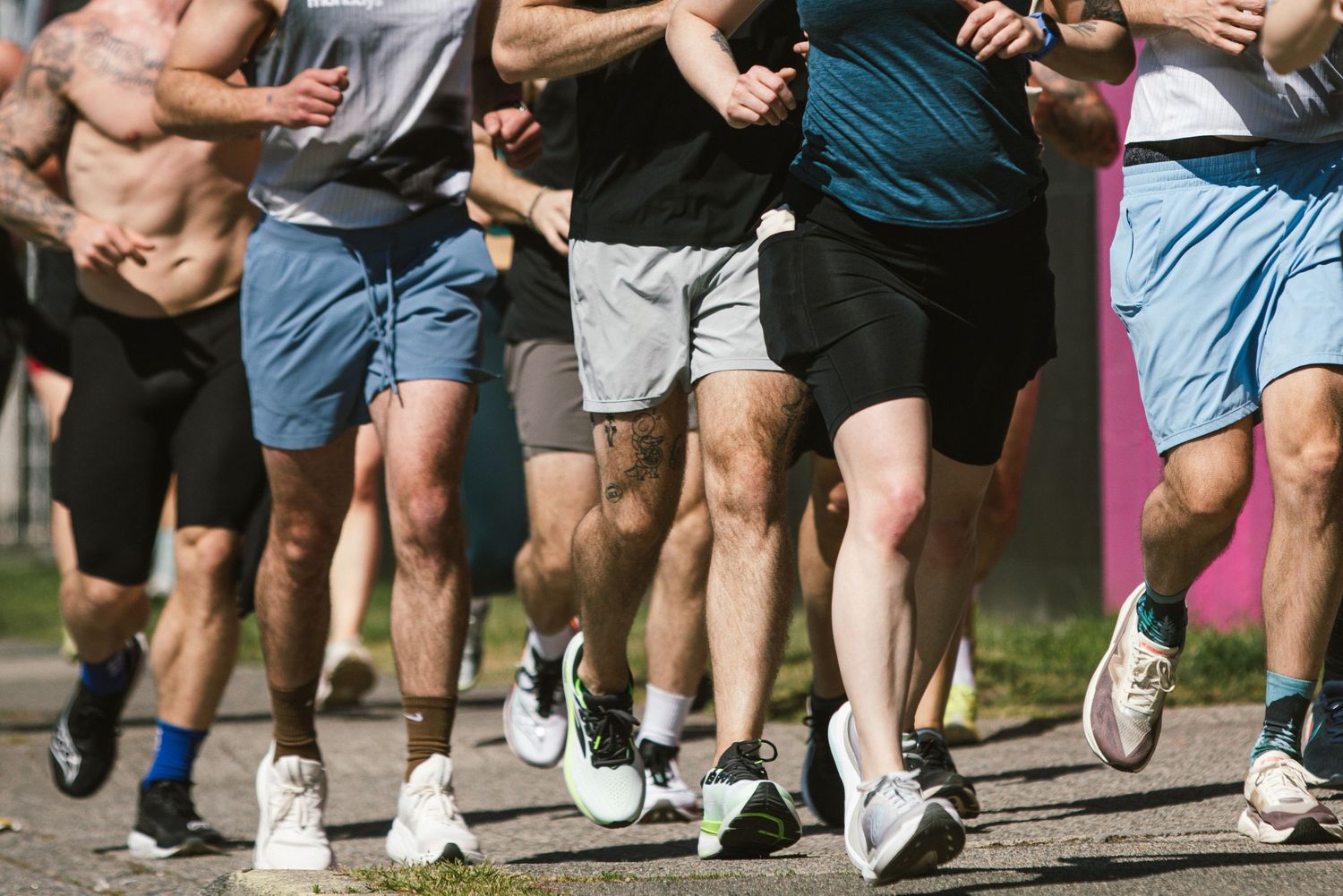 Group of runners in shorts jogging outdoors on a sunny day during a road race or group fitness run.