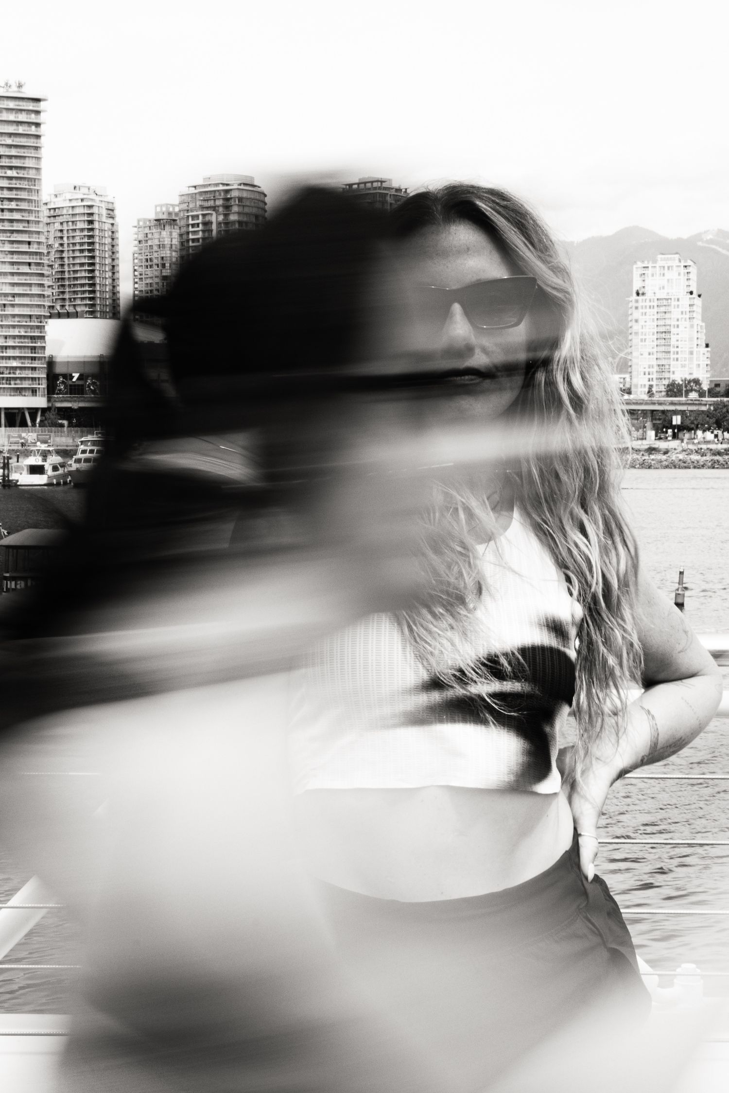 Black and white motion blur photo of woman with sunglasses near city waterfront.