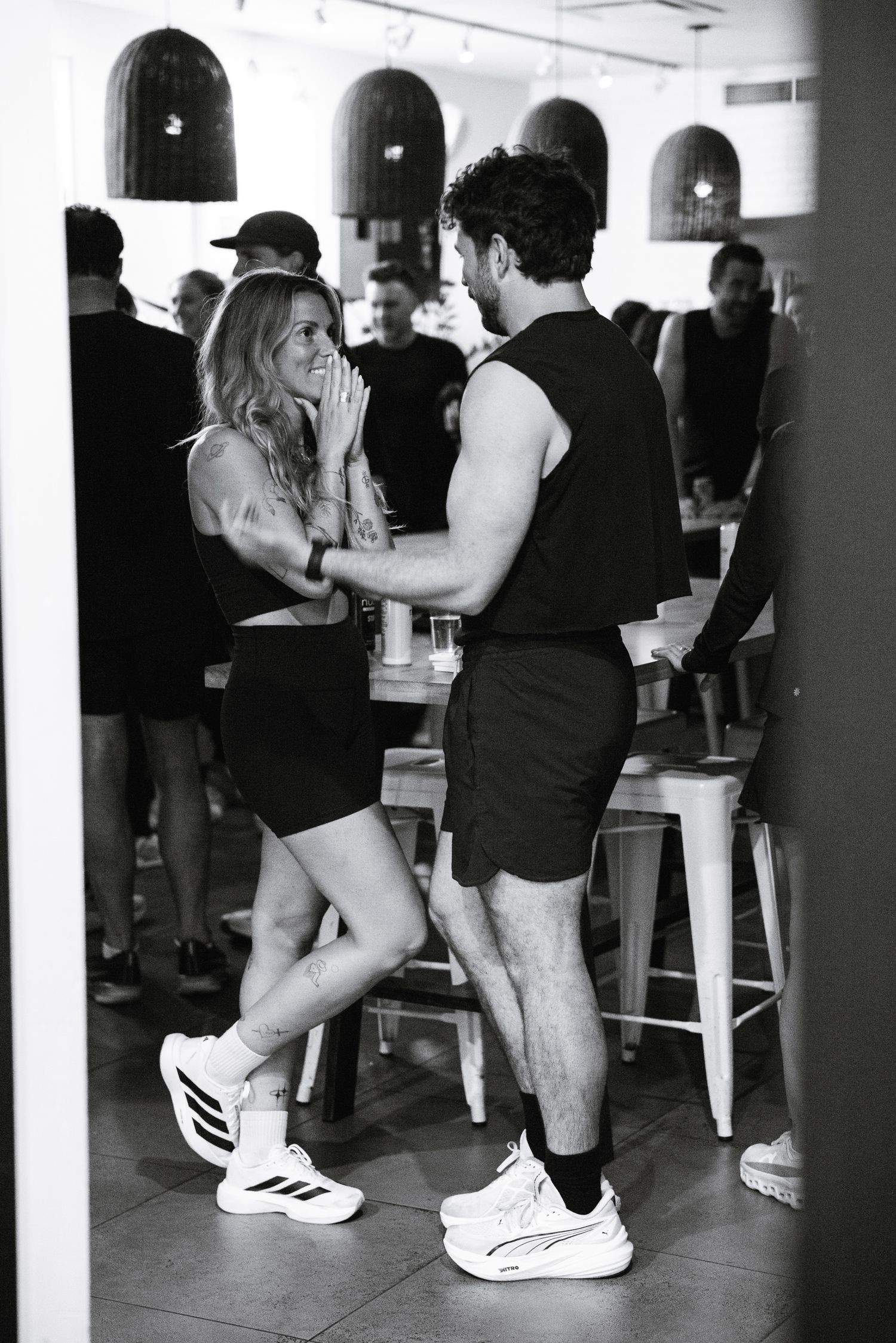 Couple in matching black athletic wear laughing together inside a casual bar.