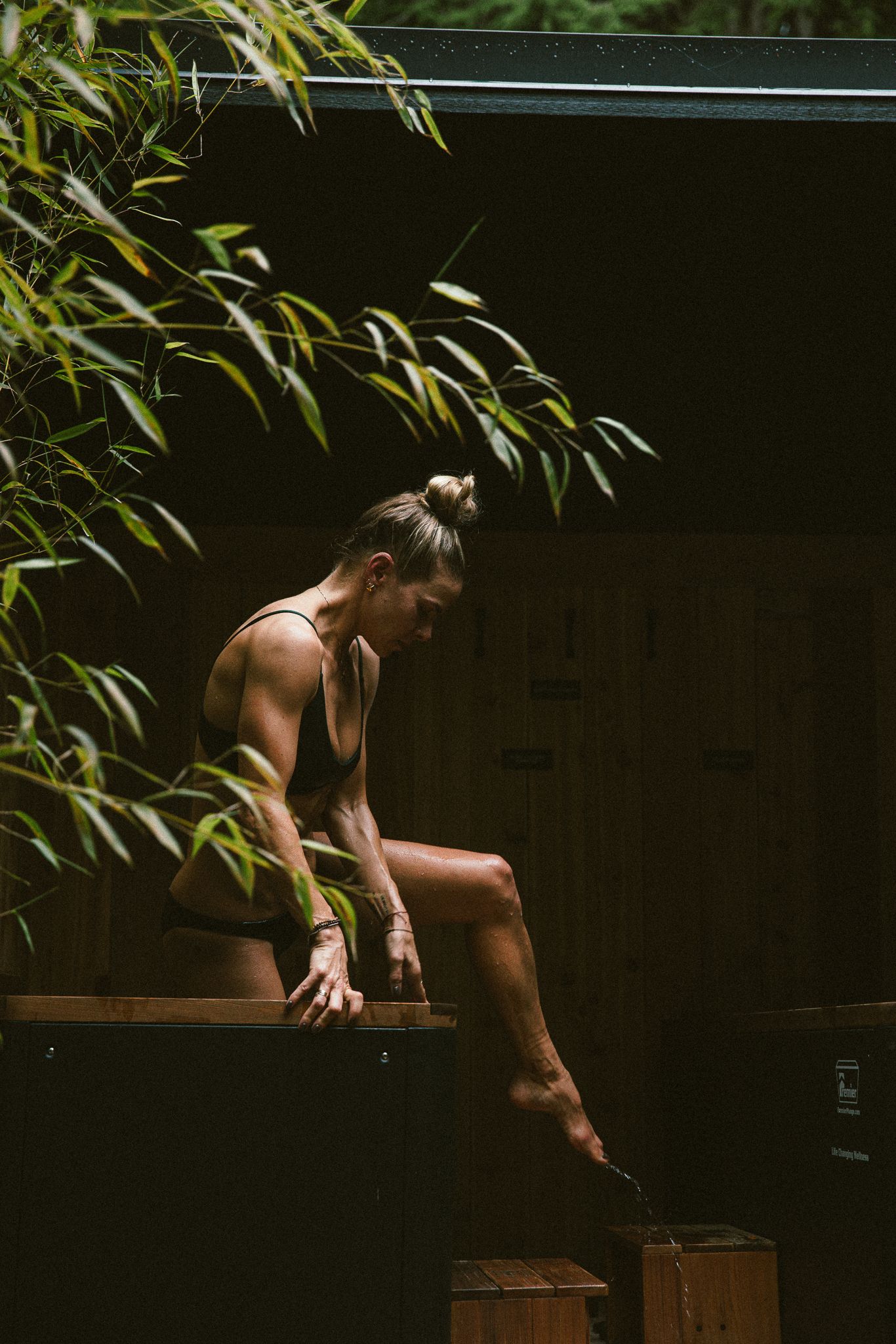 Fit woman exiting cold plunge surrounded by bamboo plants.