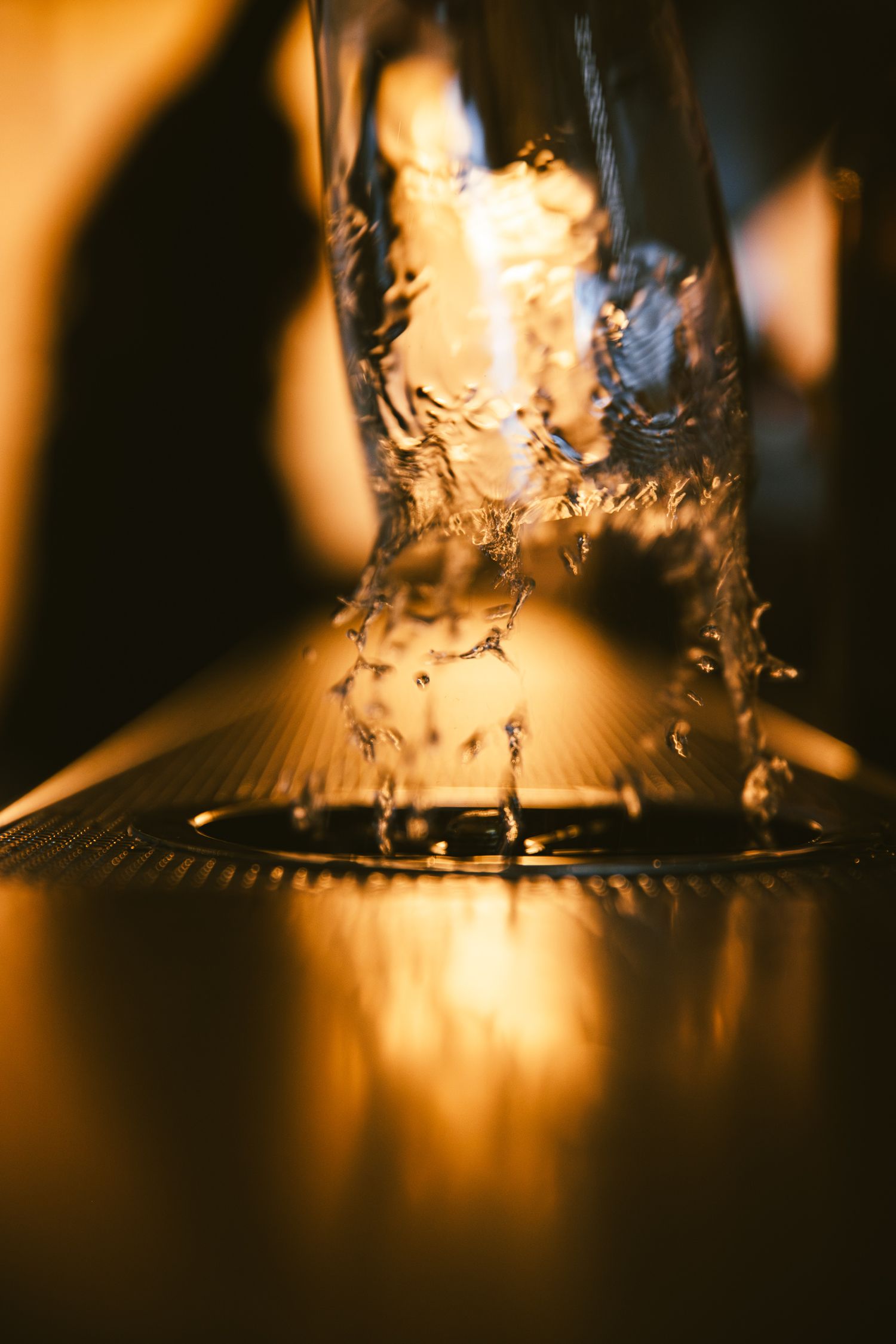 Close-up of water splashing into a glass with warm golden bokeh background in low light setting.