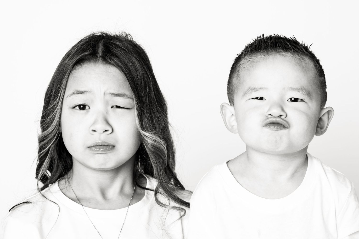 Black and white portrait of two young Asian children making funny pouting facial expressions on white background.