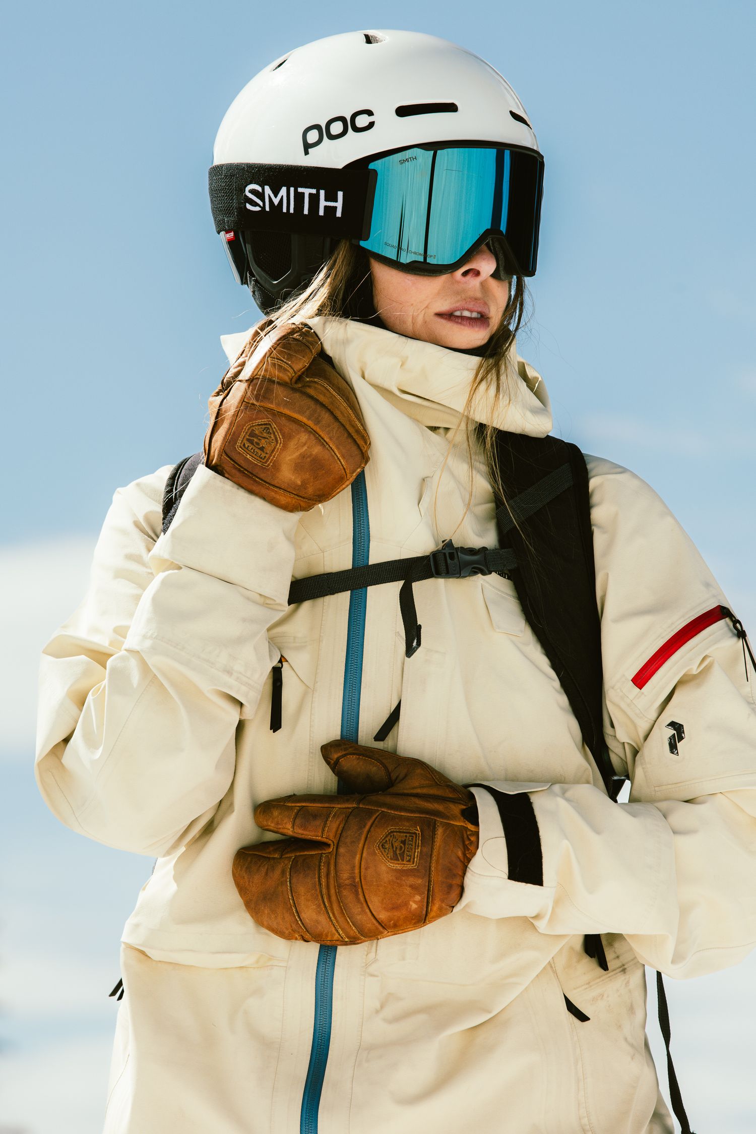 Female snowboarder in white POC helmet and Smith goggles with vintage brown leather gloves.