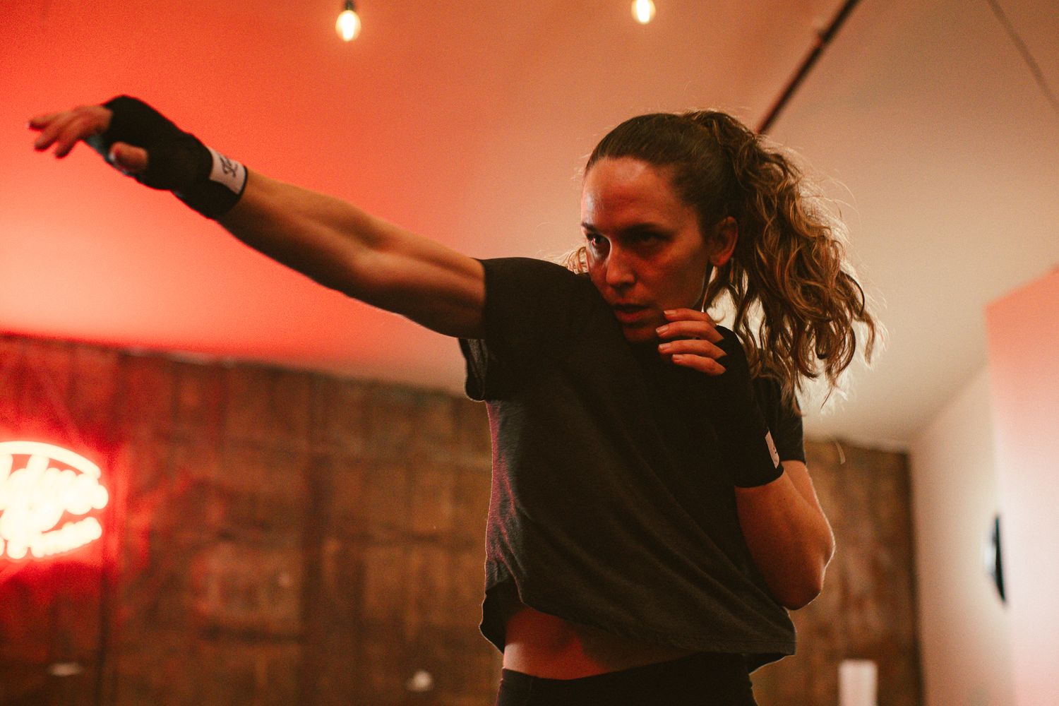 Female boxer throwing a punch during training session in red-lit boxing gym.