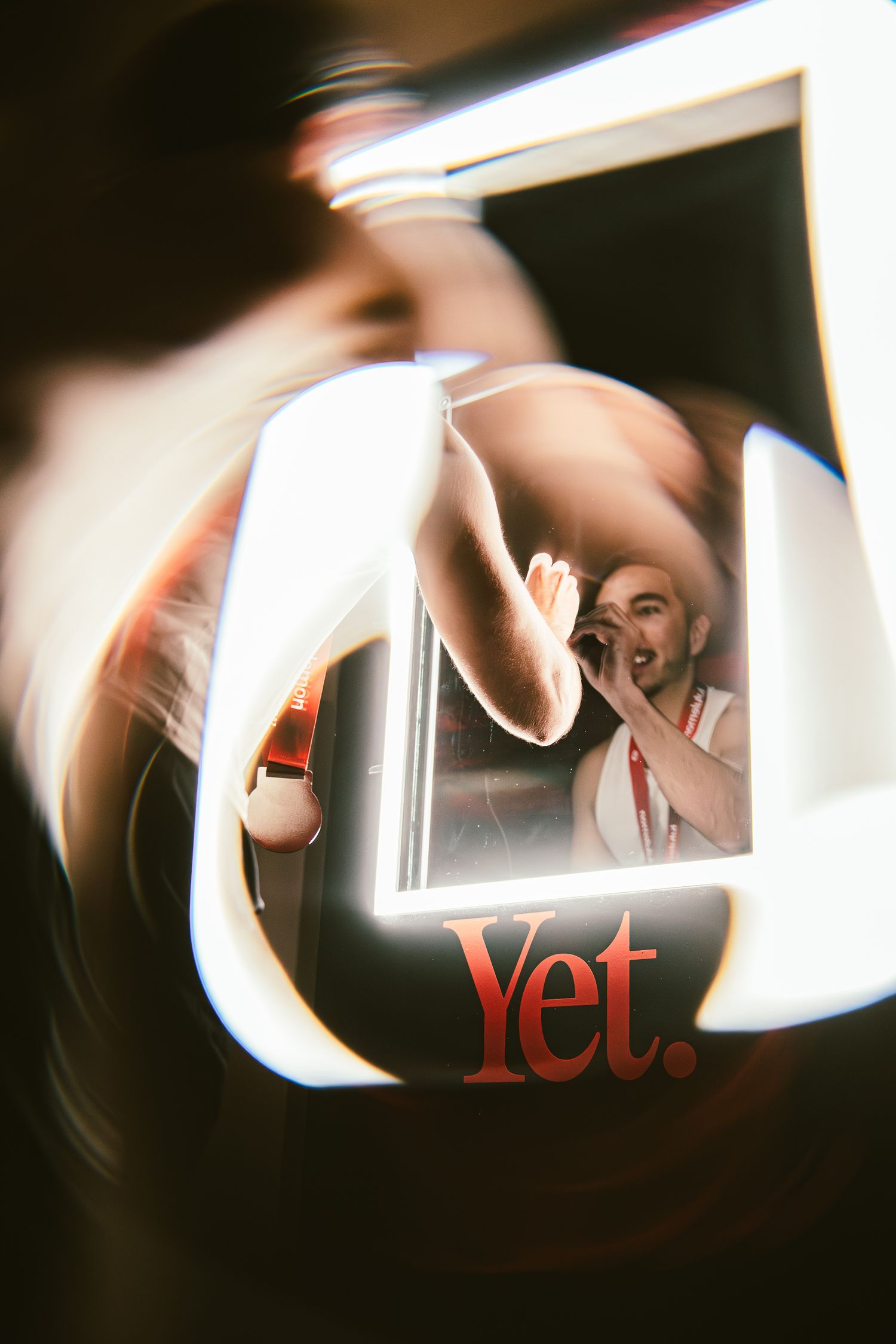 A performer singing captured in a mirror reflection with bold red Yet. text branding at a live event.
