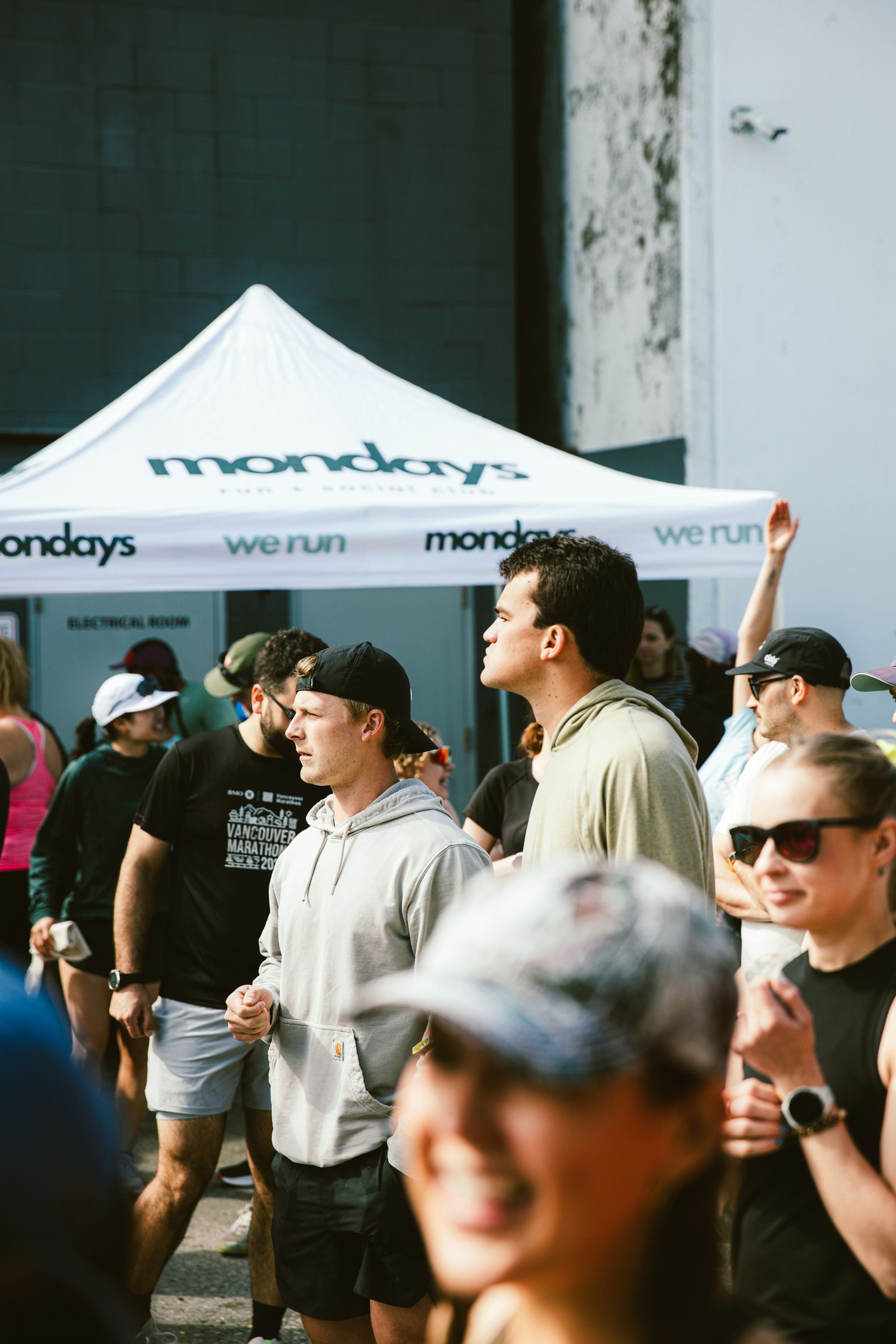 Crowd of people gathered outdoors at a Mondays We Run event under a white branded canopy tent.