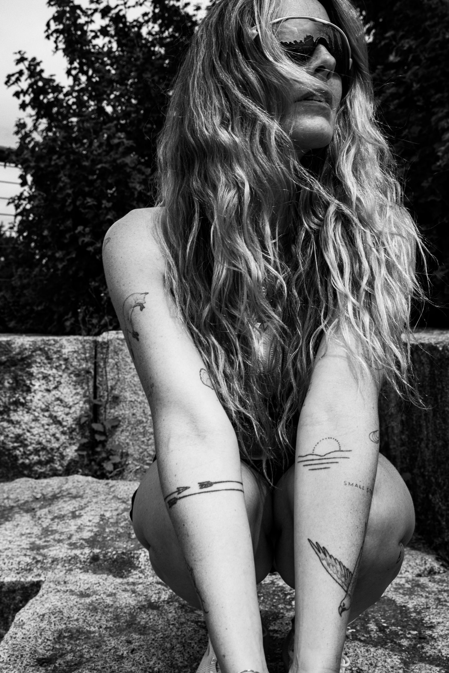 Black and white photo of tattooed blonde woman with sunglasses posing outdoors.