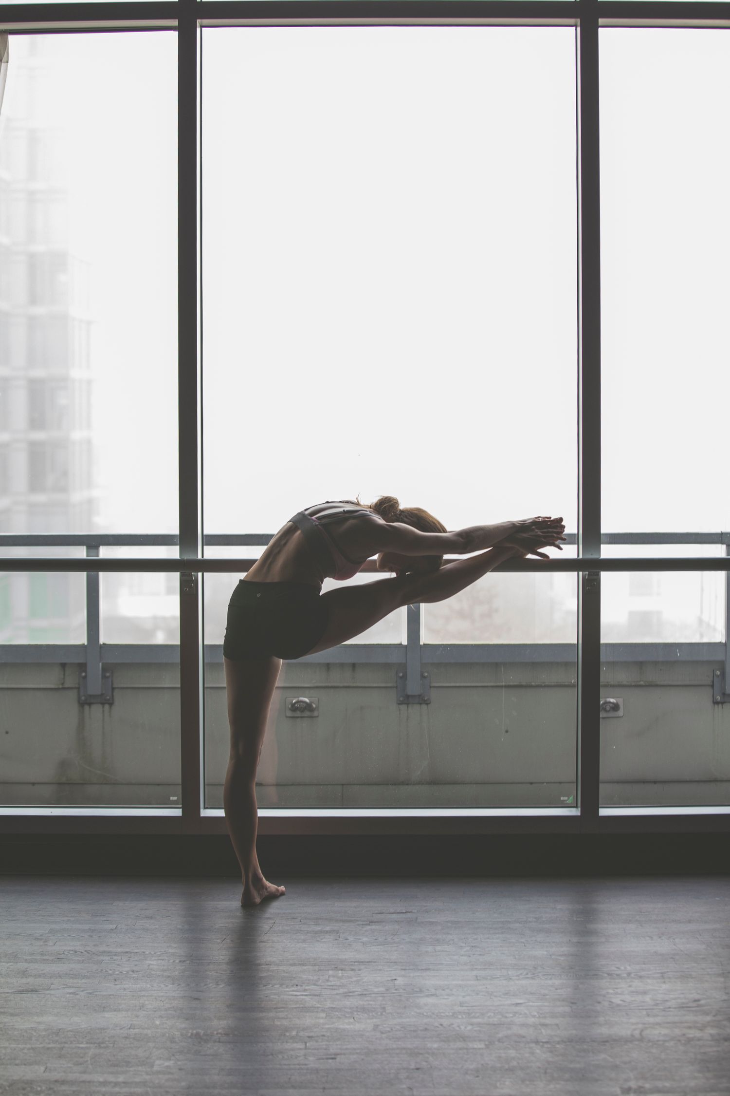 Silhouette of a flexible dancer performing a graceful backbend pose in a sunlit studio with large windows.