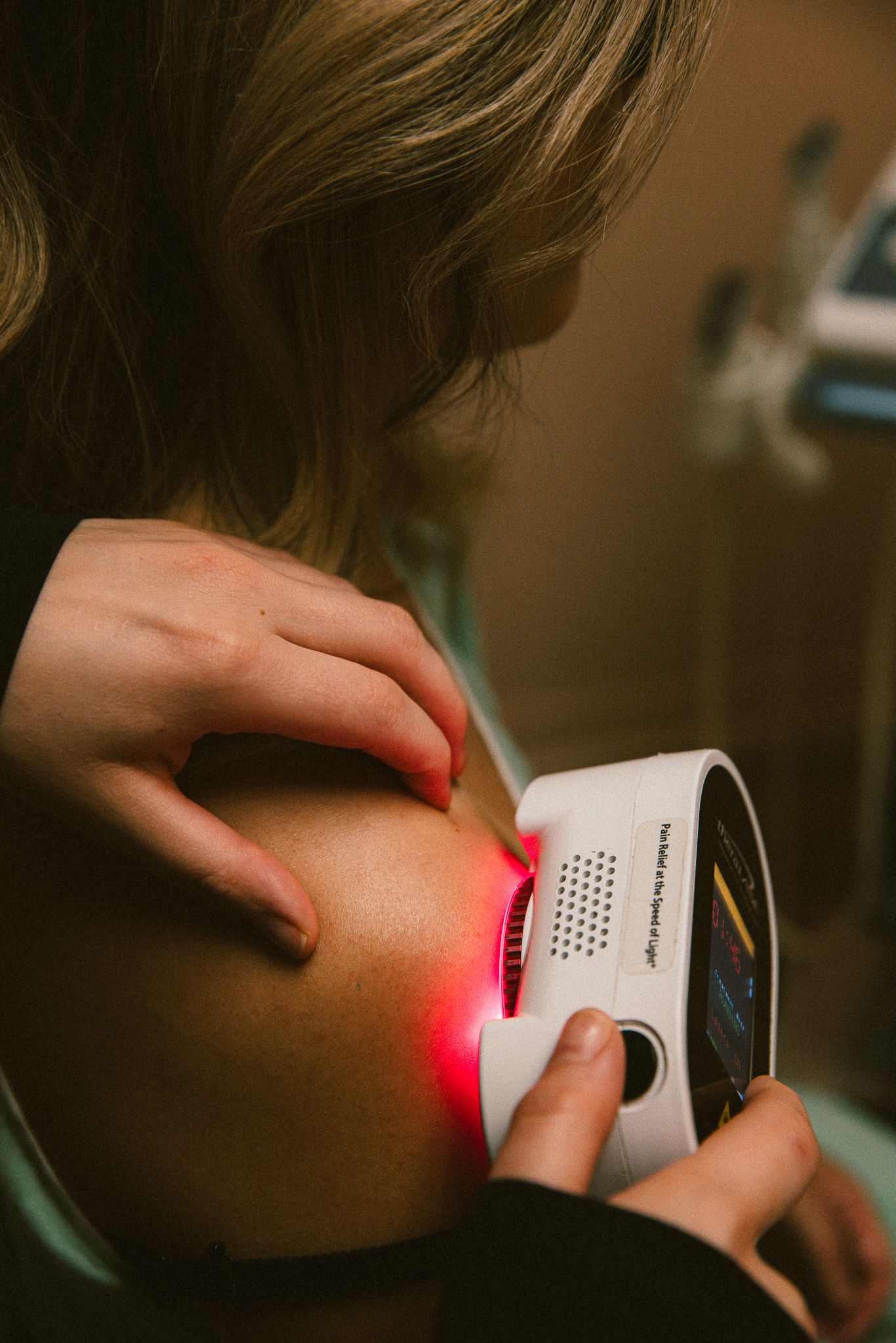 Therapist applying red light laser therapy device to patient's shoulder for pain relief treatment.