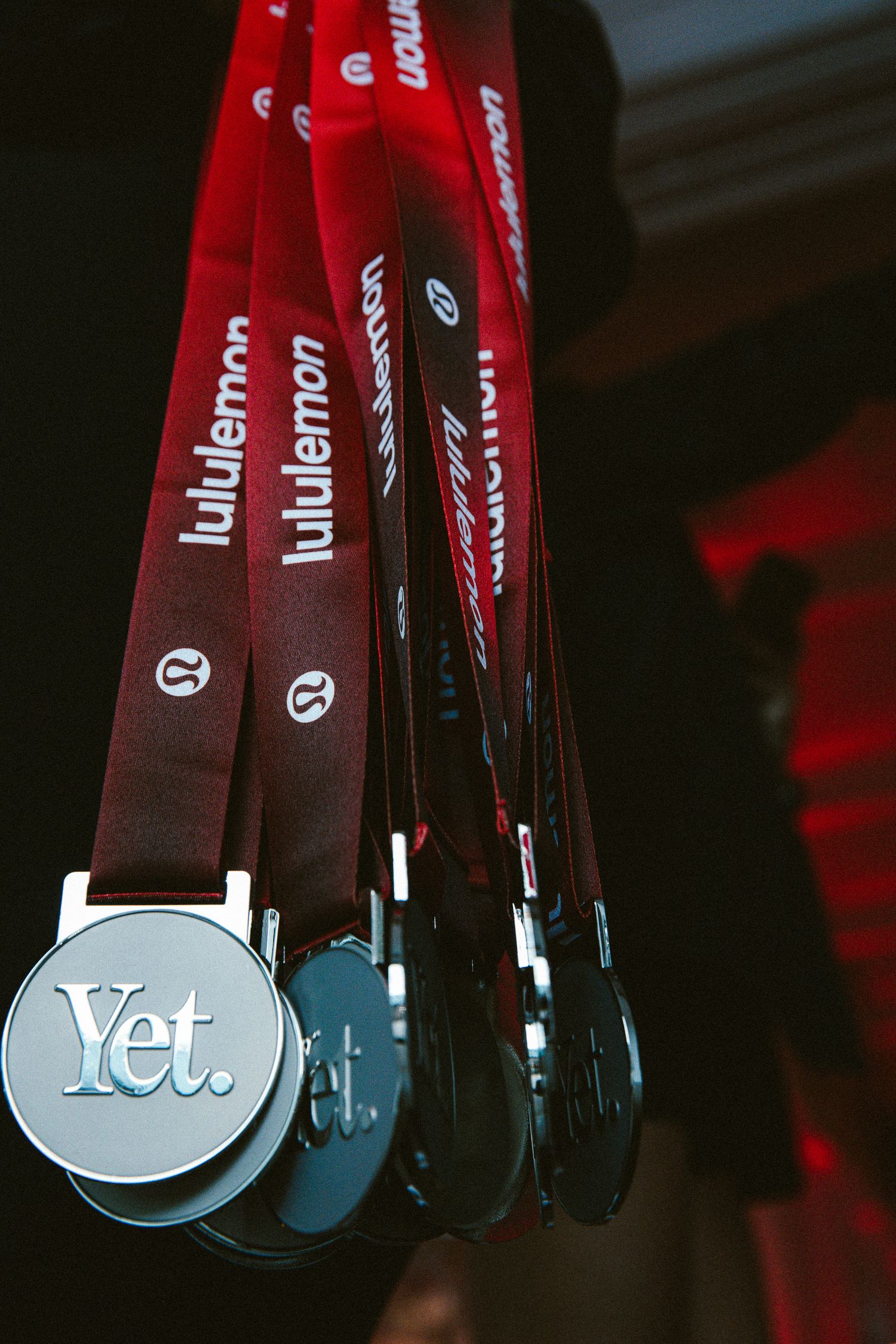 Lululemon branded red lanyards with silver Yet. medal pendants hanging in a row at a running event.