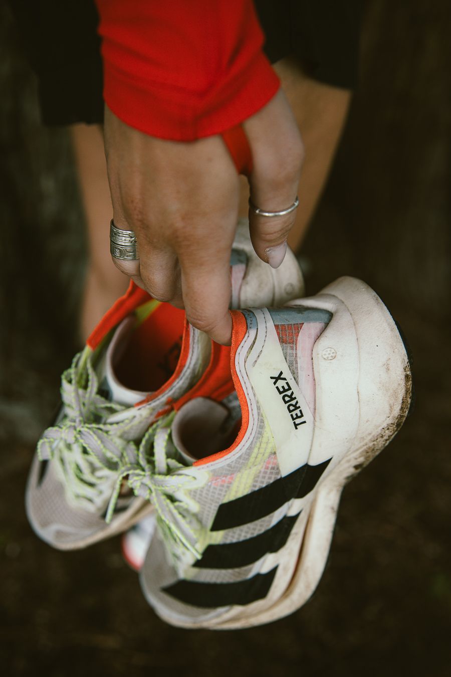 Hands holding muddy Adidas Terrex X running shoes with silver rings visible on fingers.