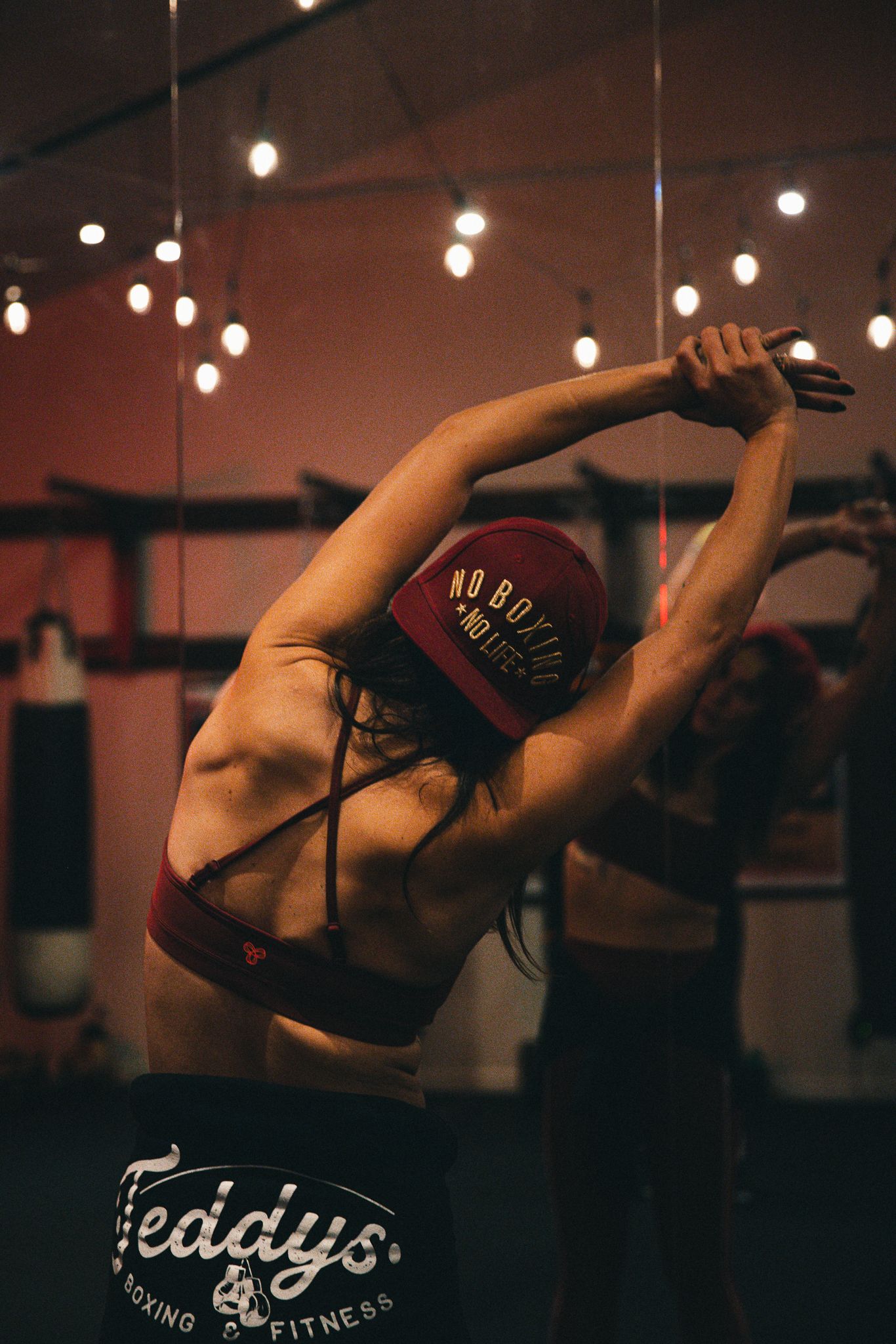 Woman stretching arms overhead at Teddys Boxing and Fitness gym with bokeh lights.