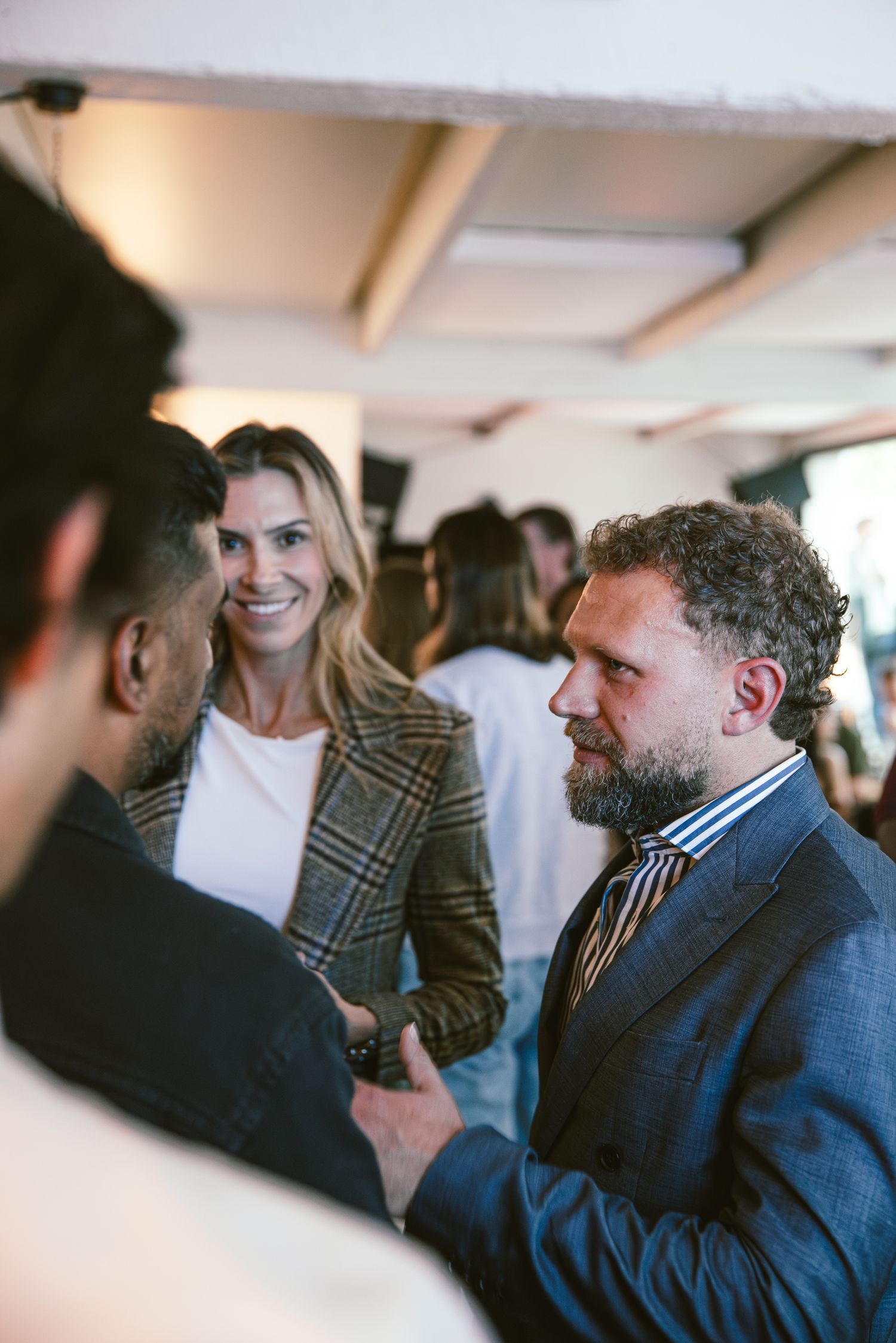 Man in suit and woman in plaid blazer networking and smiling at an indoor social gathering event.
