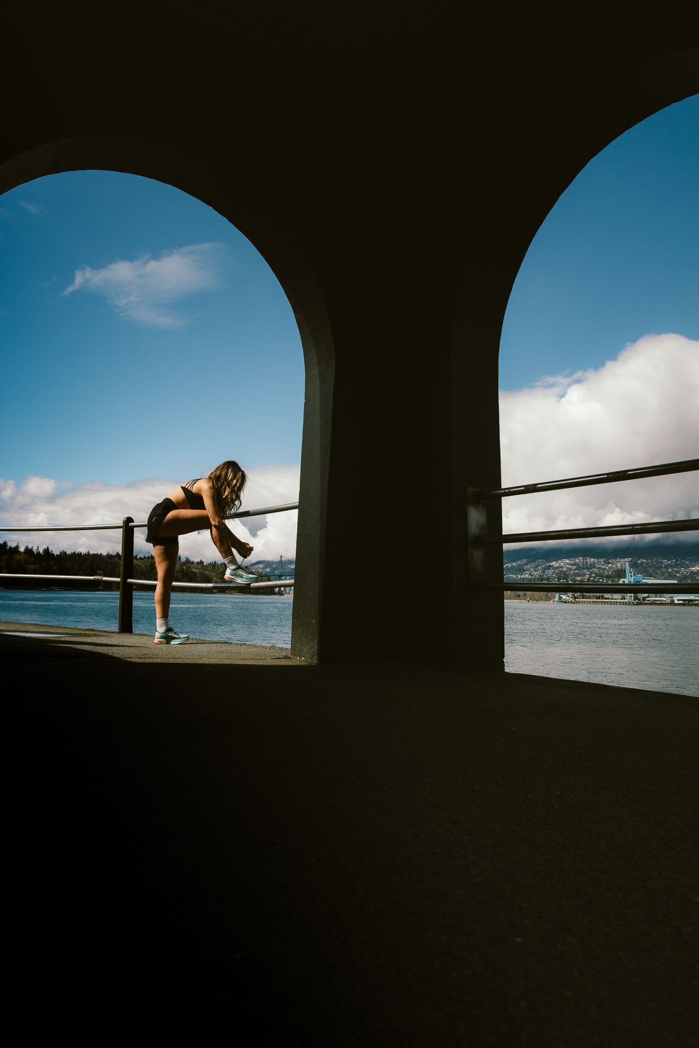 Silhouette of woman stretching by waterfront railing framed by two arched columns.