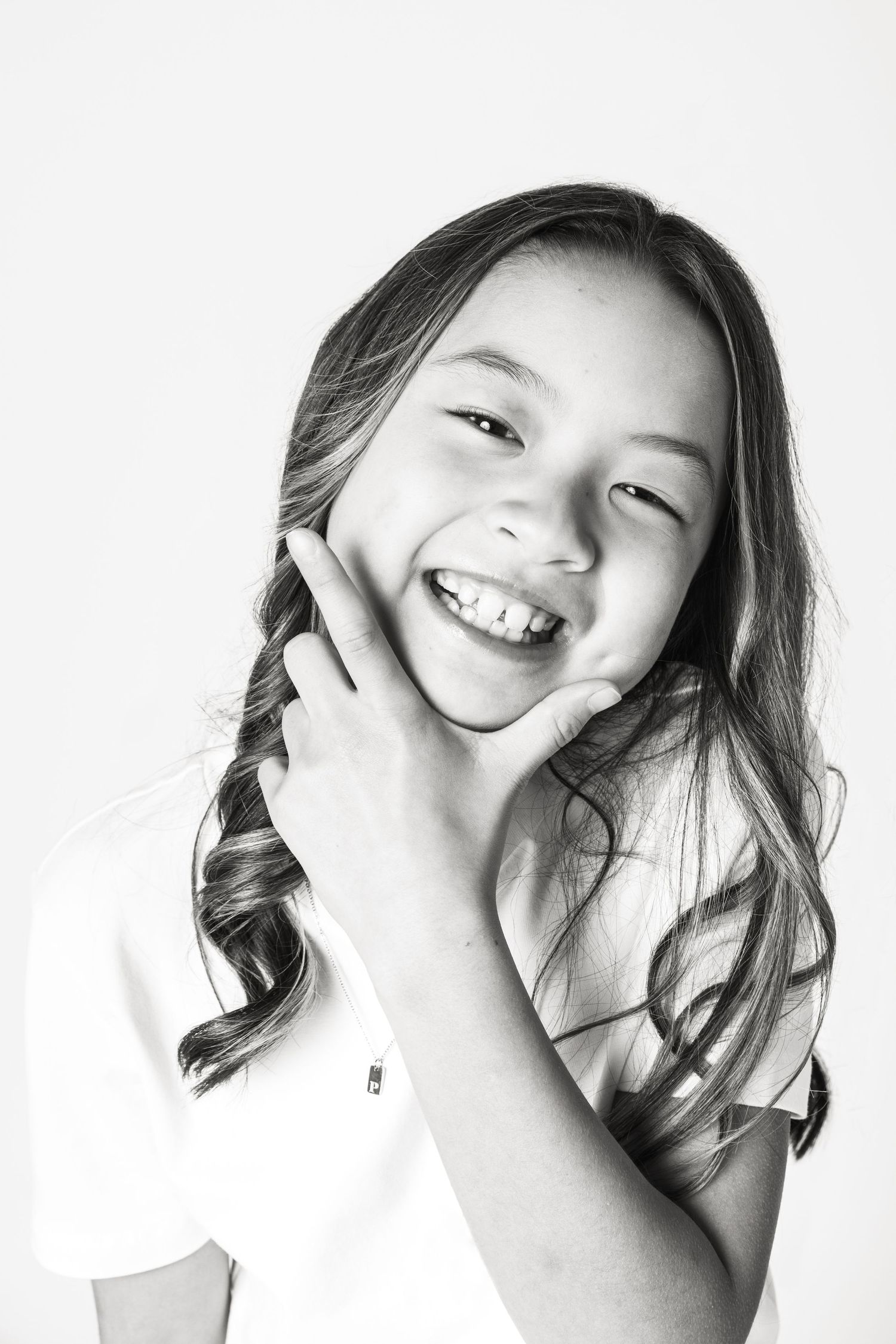 Black and white portrait of a happy young girl with long wavy hair smiling with hand on cheek.