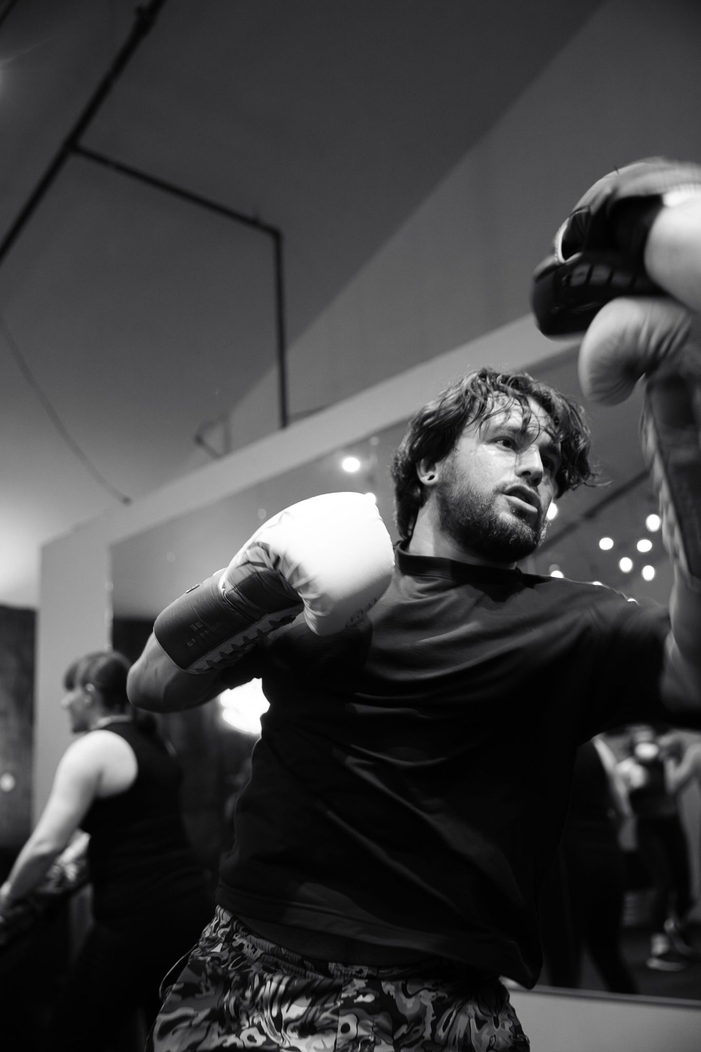 Black and white photo of a bearded male boxer throwing a punch during training in a gym.