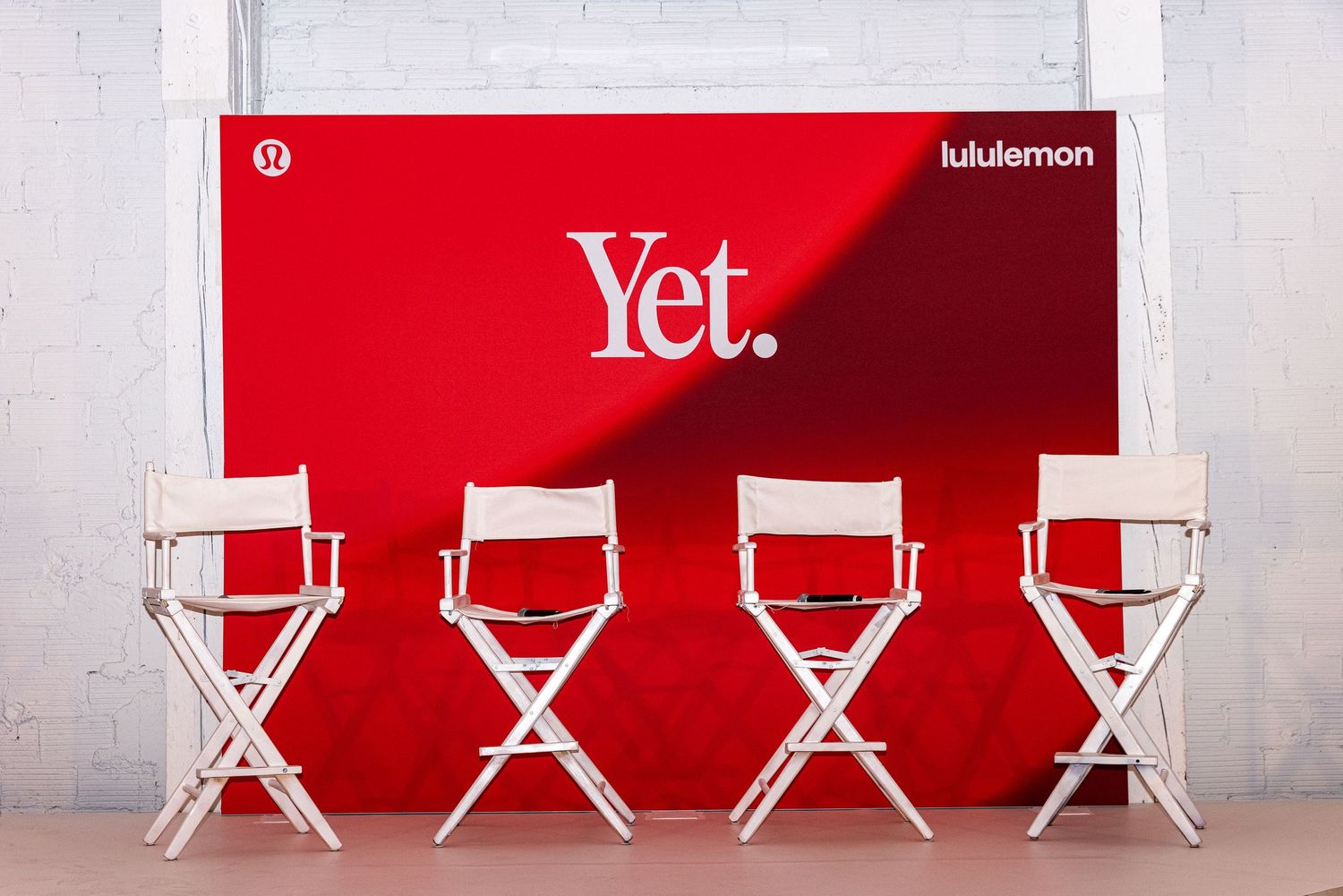Four white director chairs in front of a red Lululemon 'Yet.' branded backdrop at a promotional event.