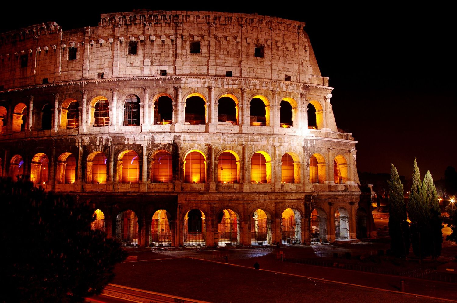 The illuminated Colosseum in Rome glows golden at night, showcasing its ancient arched facade against a dark sky.