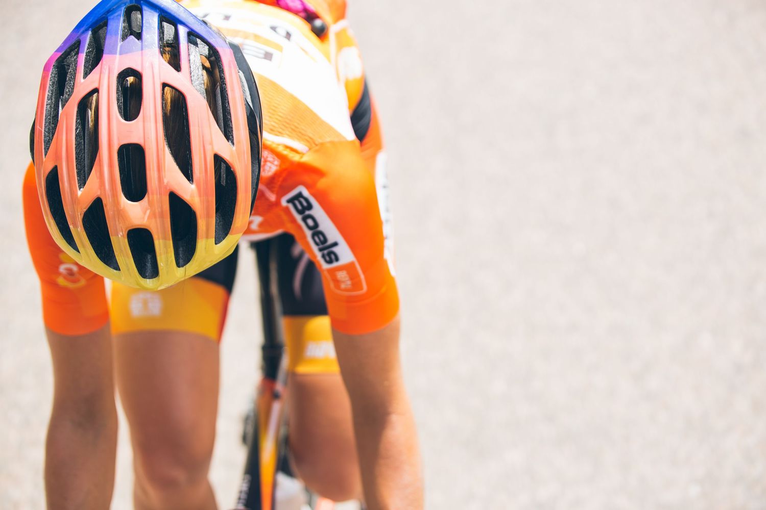 Two cyclists in orange and yellow Bael jerseys and helmets stand with their bikes on a road during a race.