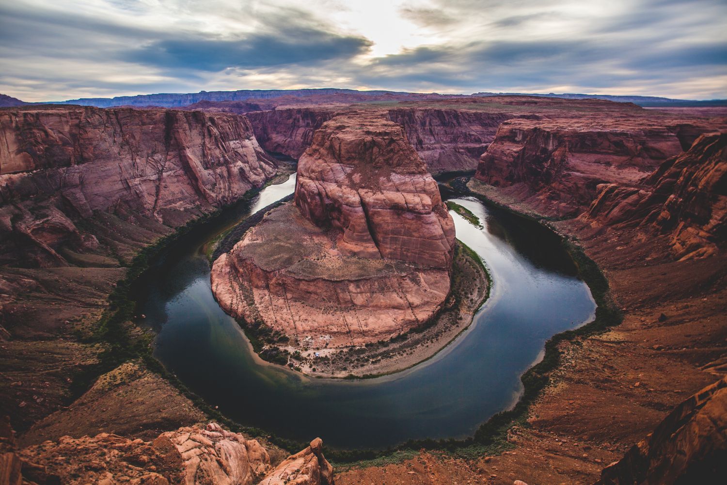 Aerial view of Horseshoe Bend, a stunning red rock canyon with the Colorado River curving below dramatic cloudy skies.