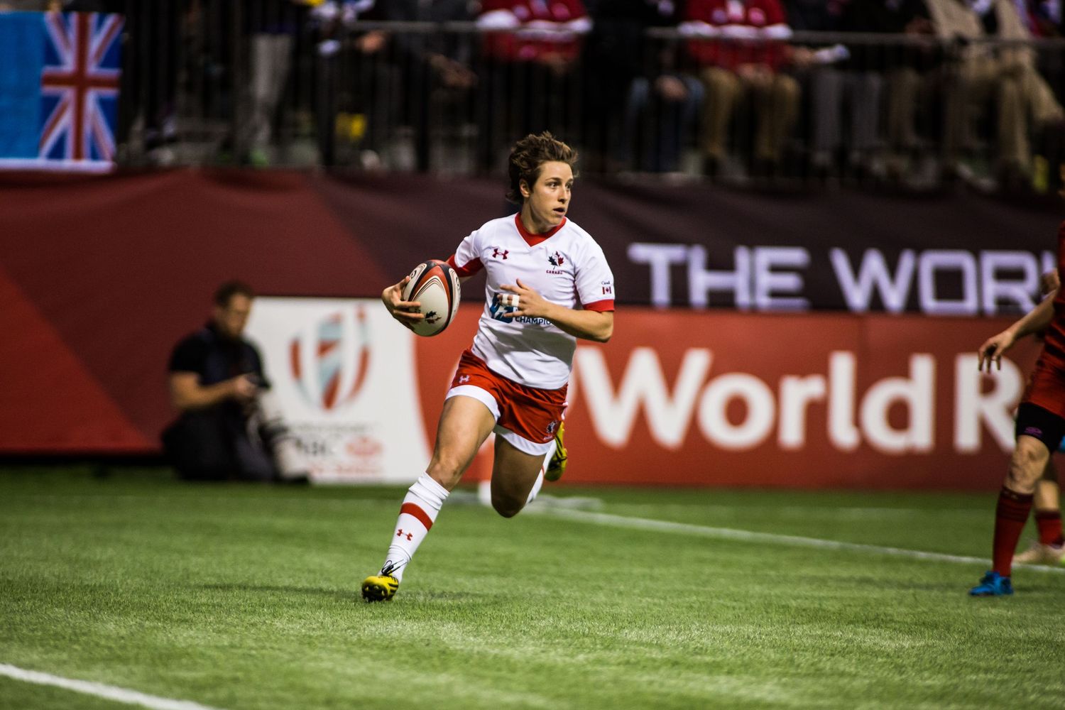 Female rugby player in red and white uniform sprints with ball during World Rugby Sevens Series match.