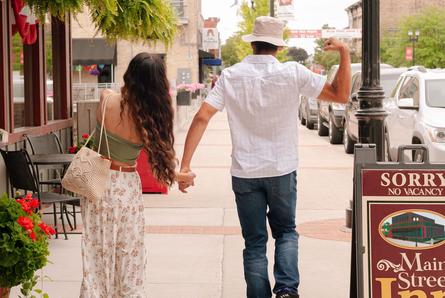 Couple holding hands walking down a charming small-town Main Street sidewalk on a sunny day.