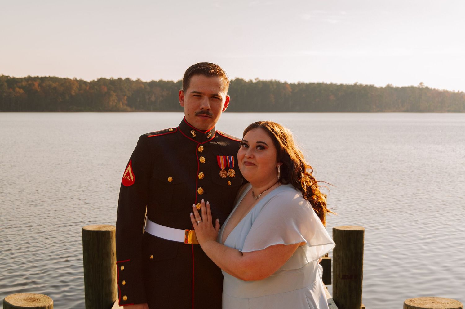 A couple poses on a dock, man in Marine Corps dress blues, woman in white top smiling.