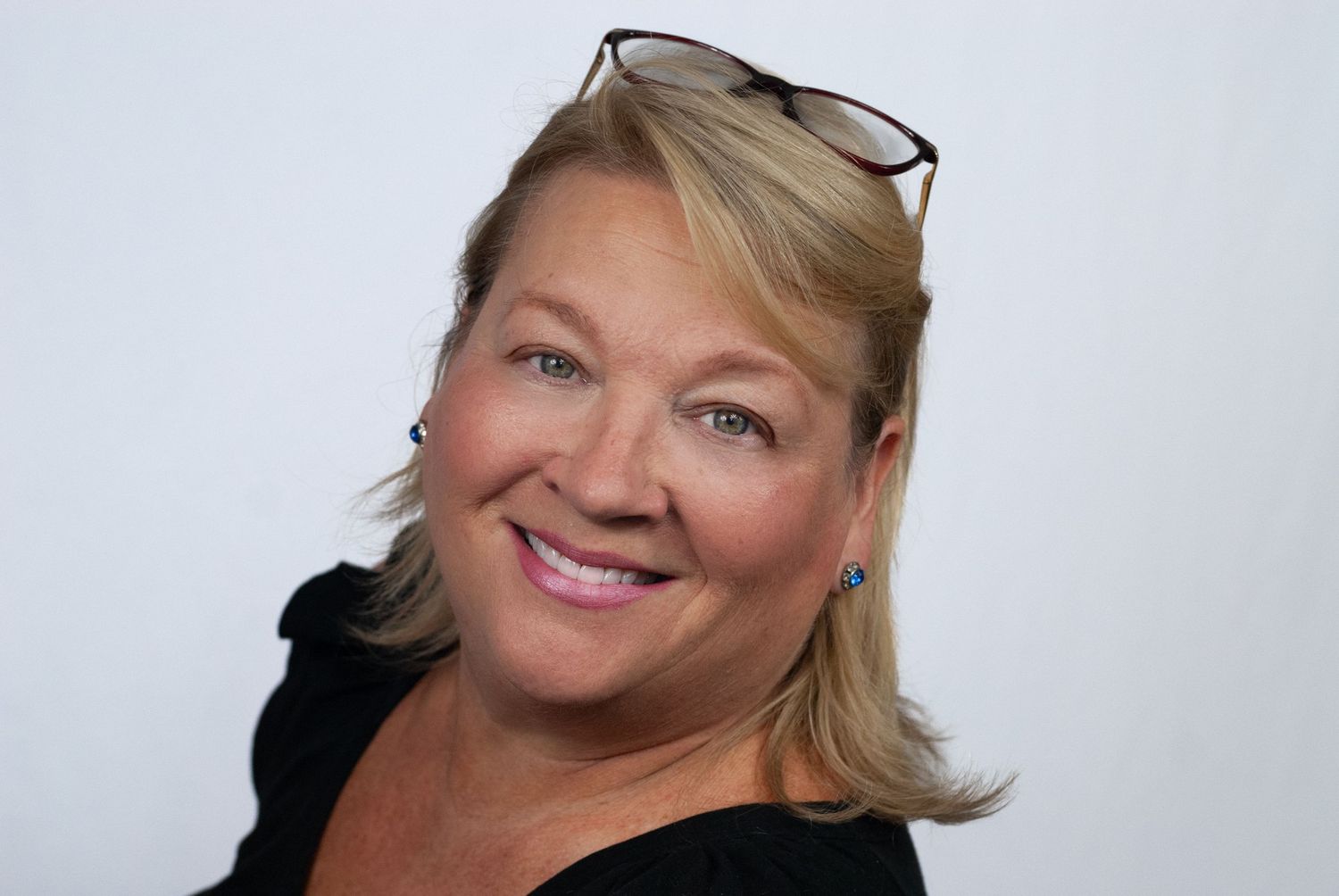 Cheerful blonde woman with black-rimmed glasses on her head smiling in a professional headshot.