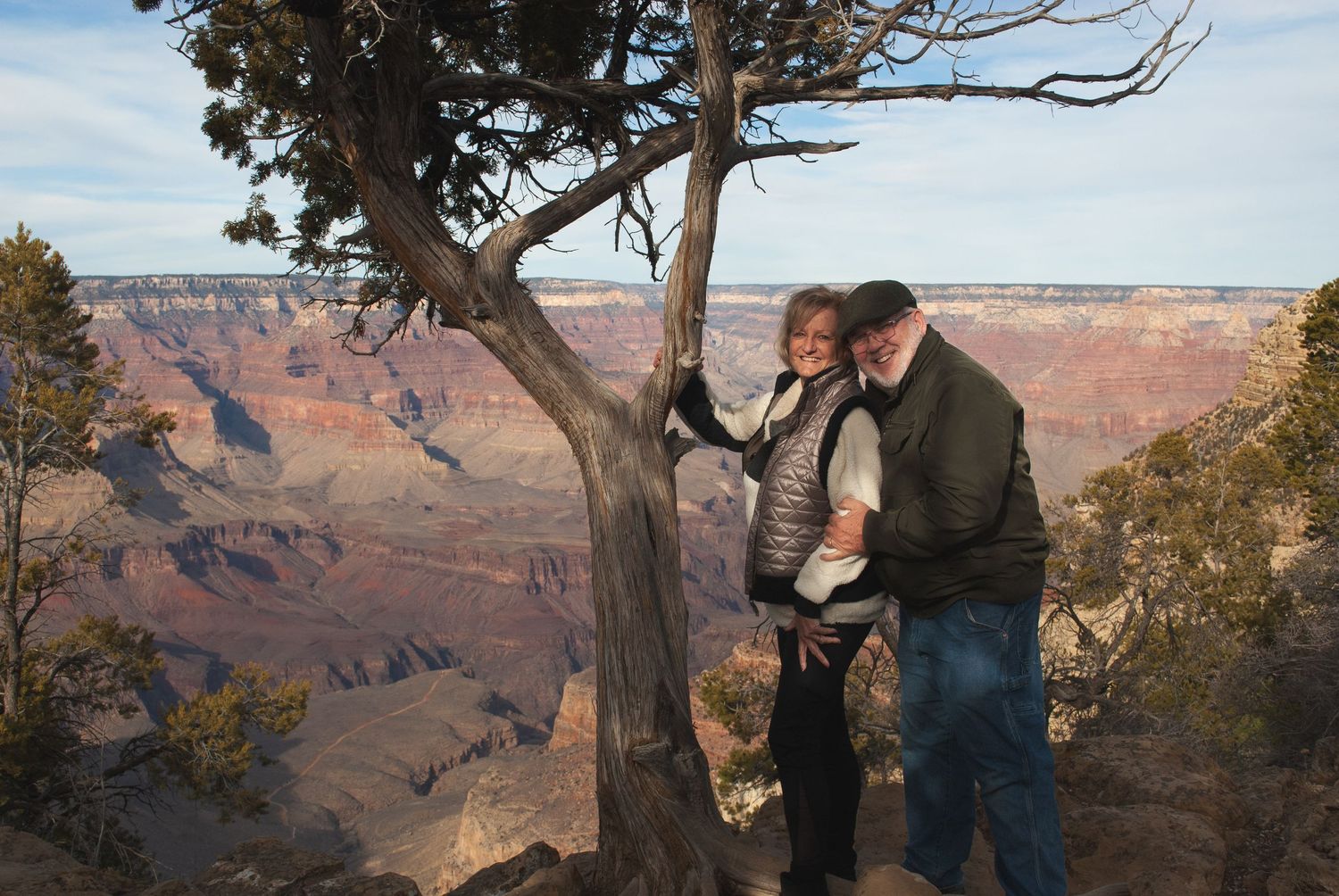 Couple embracing by a tree at the Grand Canyon with stunning red rock canyon views behind them.