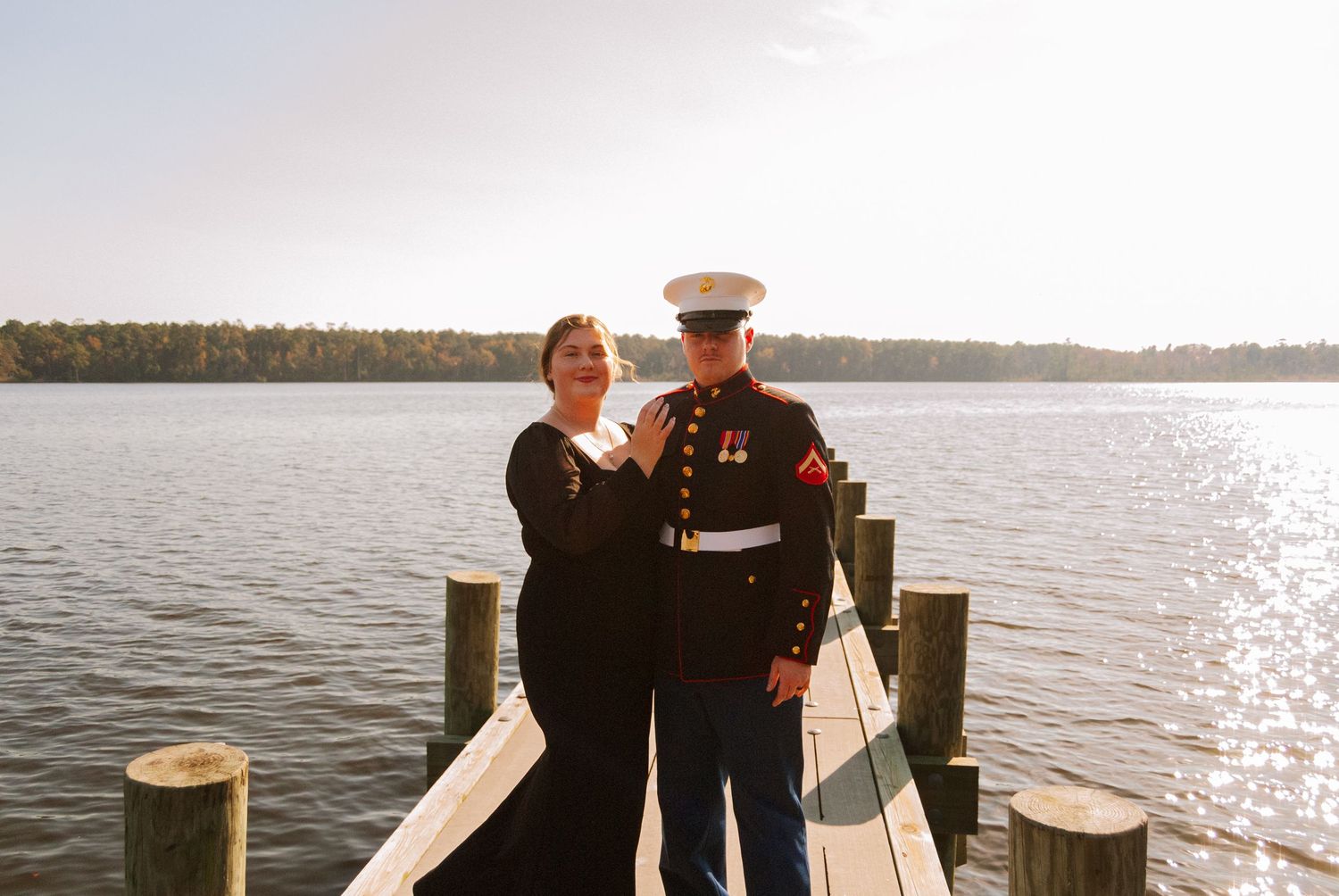 Marine in dress uniform posing with partner on wooden dock at sunset by lake.