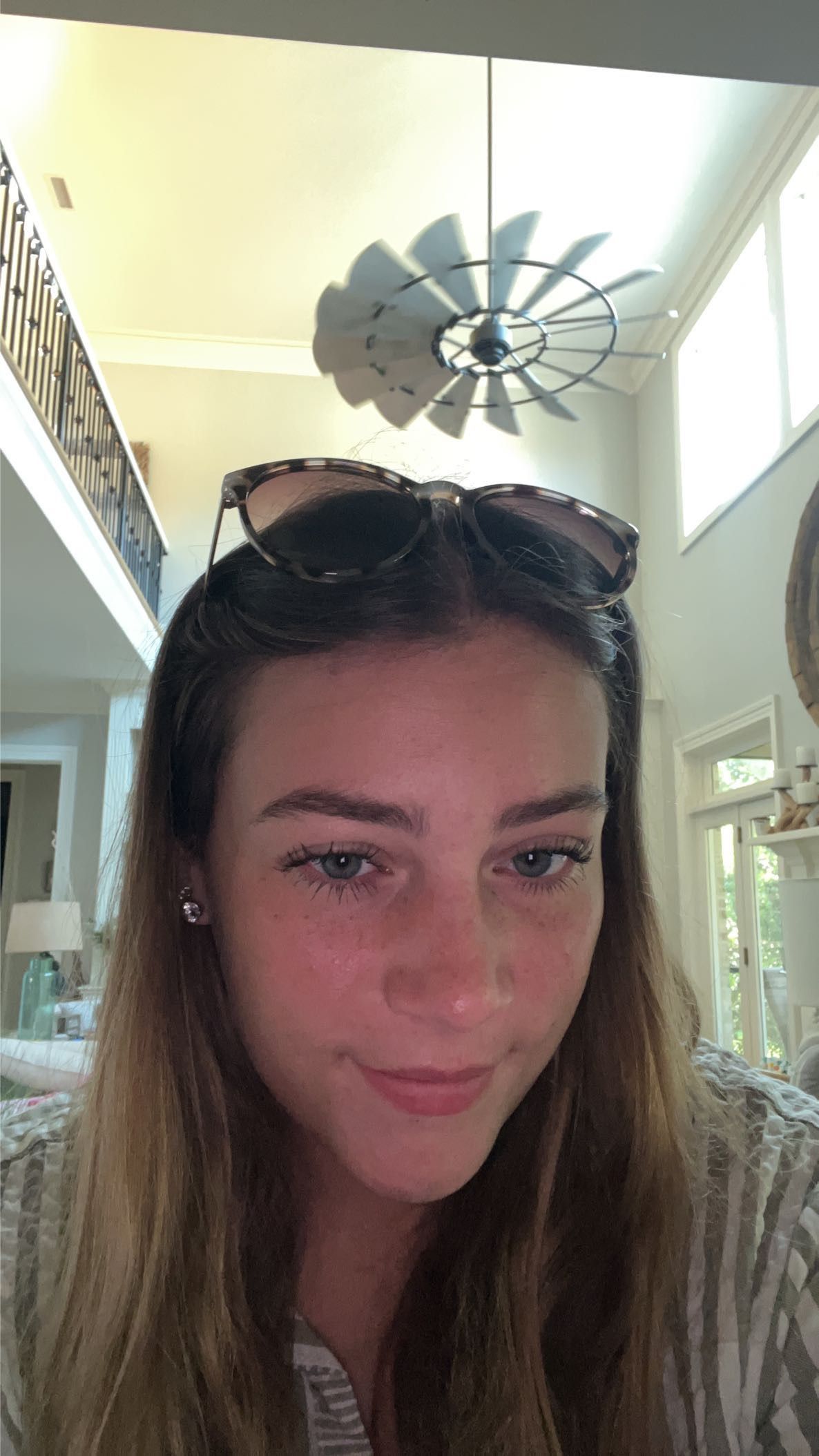 Young woman with sunglasses on her head smiling indoors near a windmill ceiling fan.