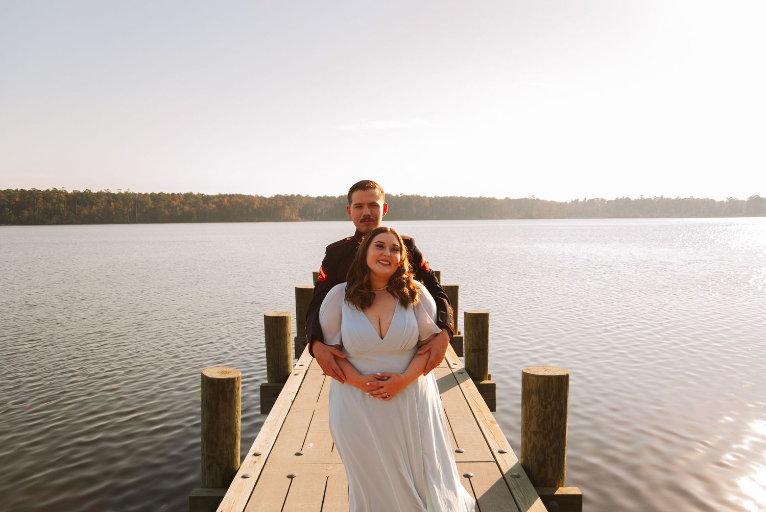 A couple embraces on a wooden dock overlooking a calm lake surrounded by autumn trees.