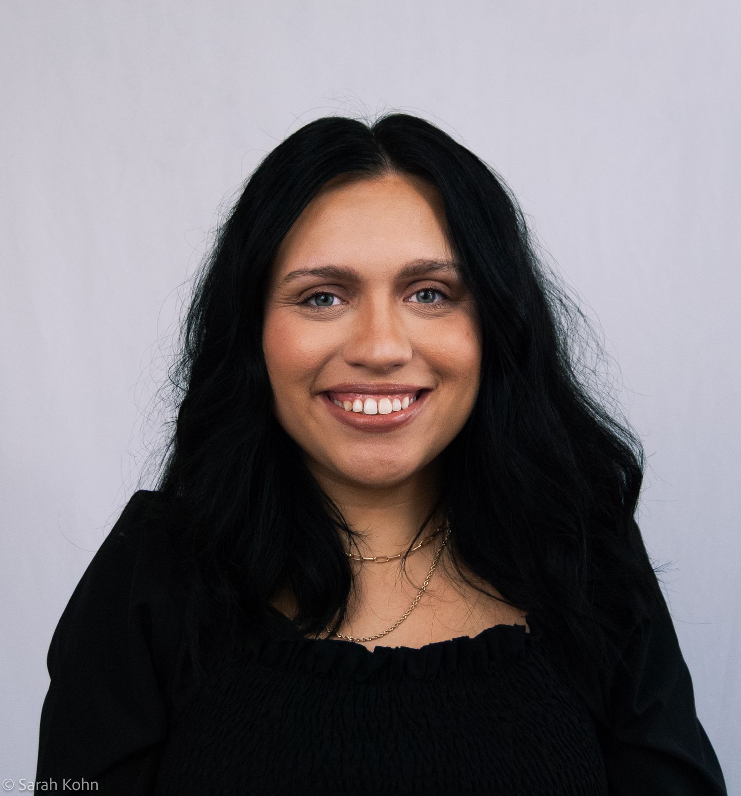 Smiling woman with long black hair wearing a black top, professional headshot photo.