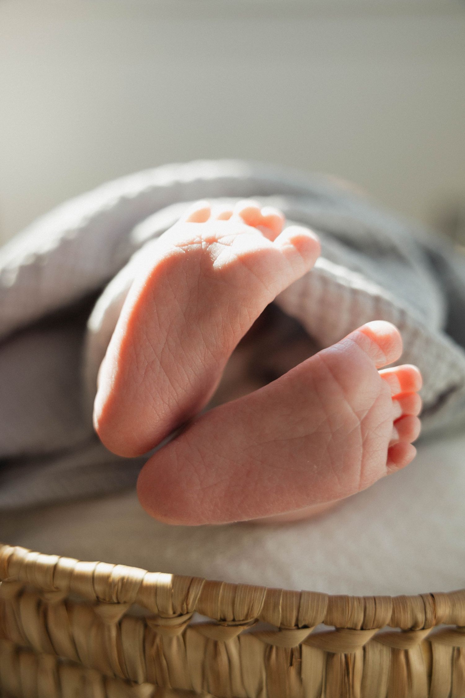 Newborn baby feet peeking out from a gray blanket in a wicker basket.