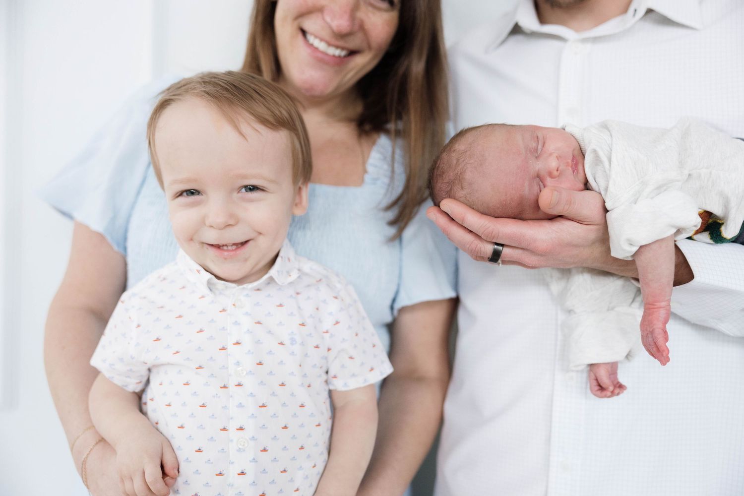 Smiling family with toddler boy and newborn baby posing together indoors.