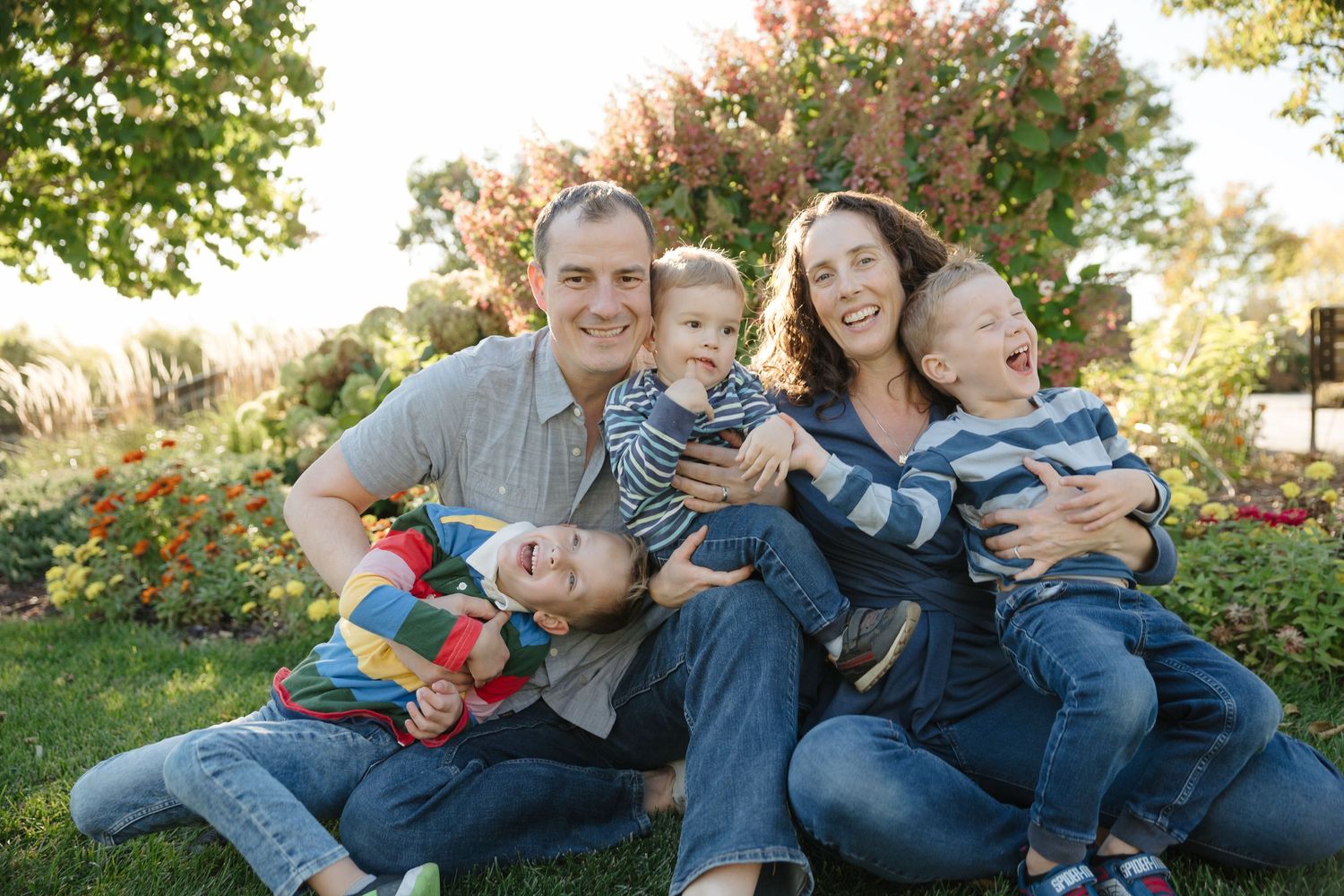 Joyful family of five laughing together outdoors in colorful garden with parents holding three young children.