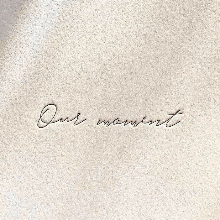 Cursive embroidered text reading Our moment on a soft cream fabric surface.