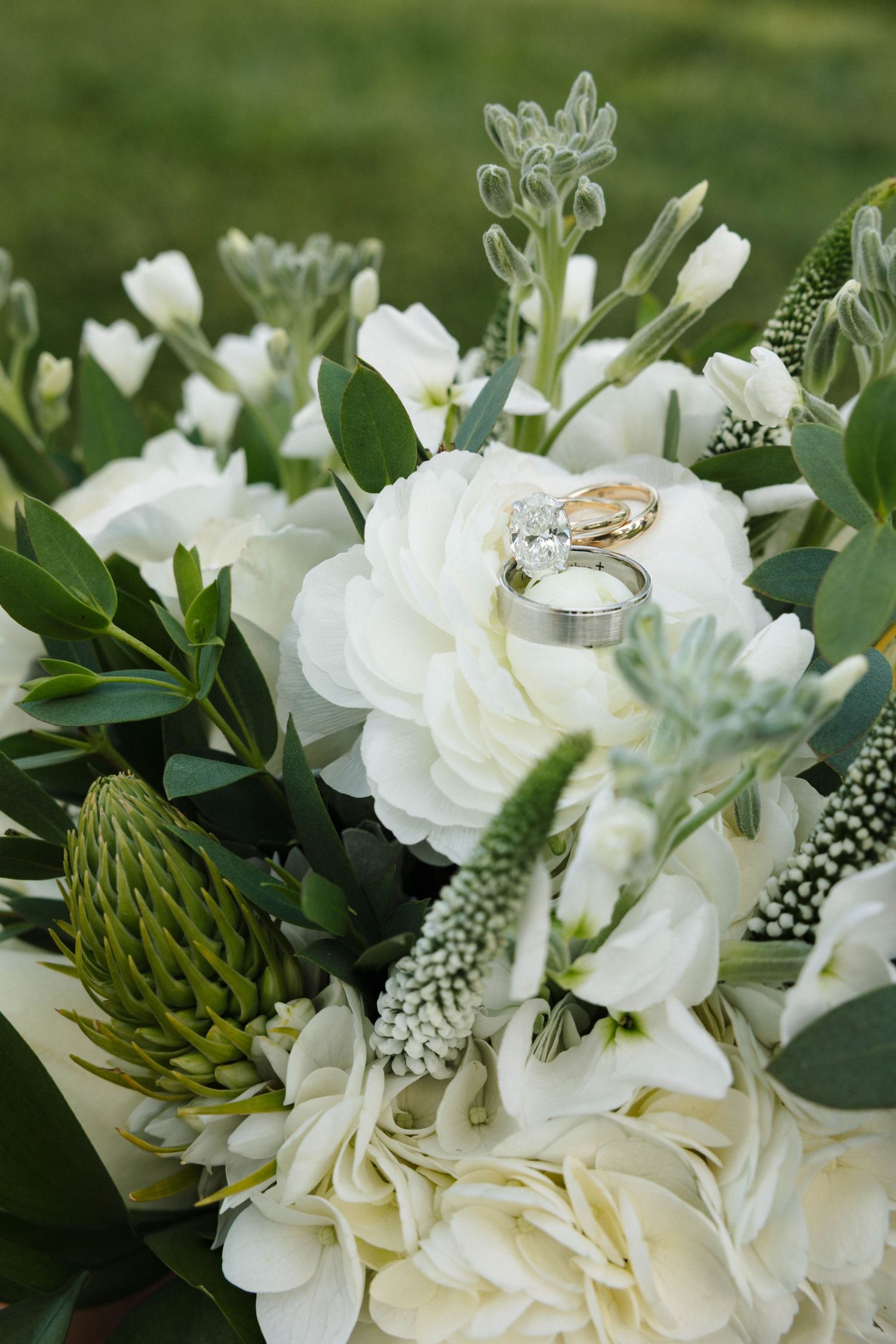 Wedding rings resting on a lush white bridal bouquet with greenery and hydrangeas.