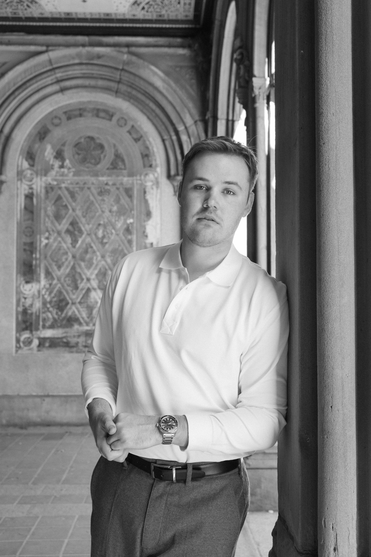 Black and white portrait of man in white shirt leaning against column at Bethesda Terrace, Central Park.
