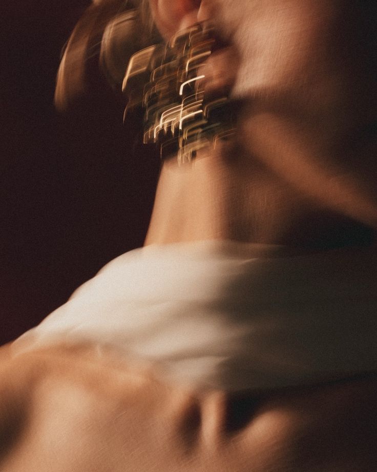 Artistic blurred close-up portrait of a person wearing a gold geometric necklace in dramatic lighting.