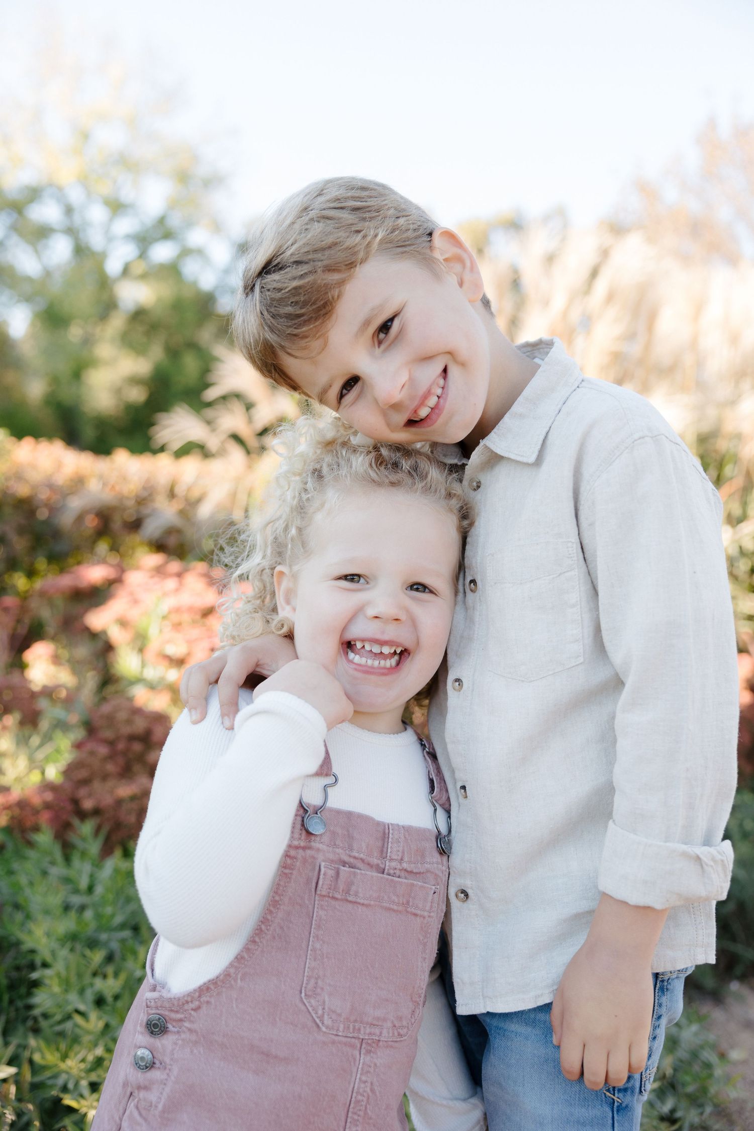 Smiling boy hugging his curly-haired little sister in an autumn garden.