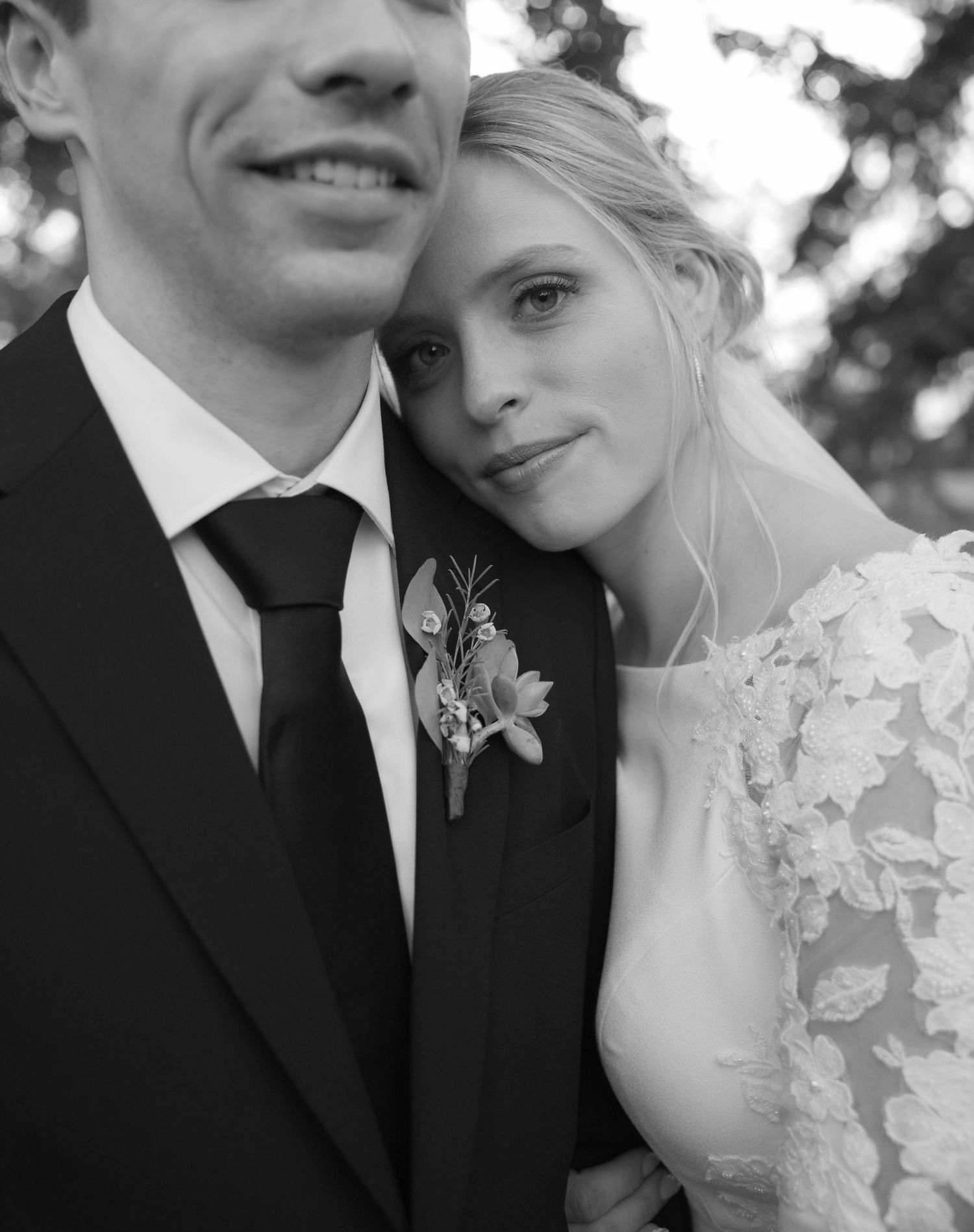 Black and white portrait of bride leaning on groom wearing black tie and boutonniere.