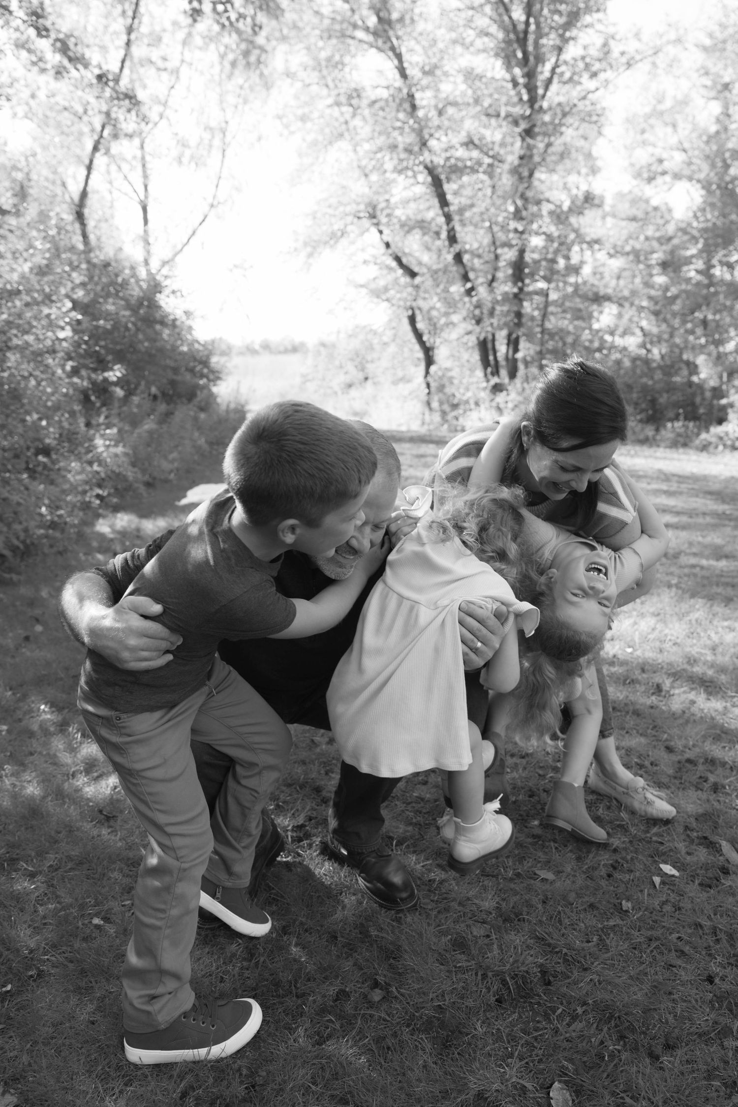 Black and white candid photo of children playfully hugging outdoors surrounded by trees.