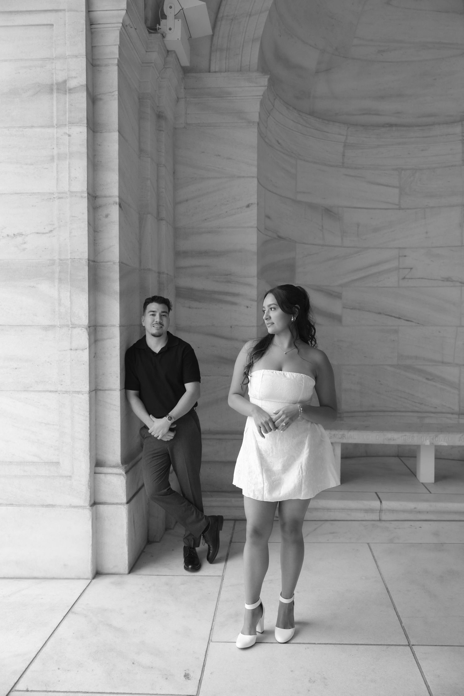 Couple posing separately beneath marble arched columns of a neoclassical building, black and white portrait.